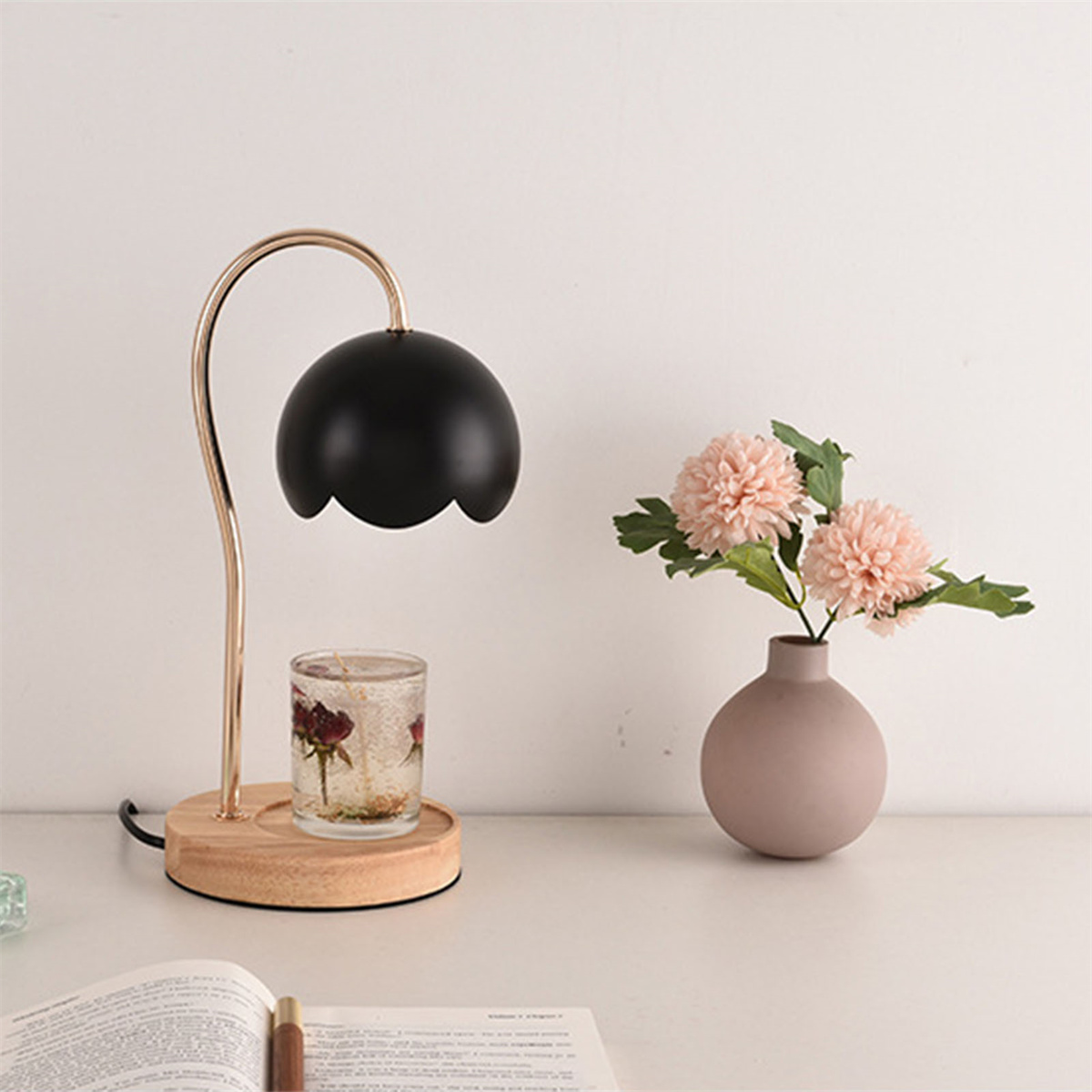 Schwarze Lampe mit floralem Schirm, Vase mit Blumen, offenes Buch. Weiße Oberfläche.