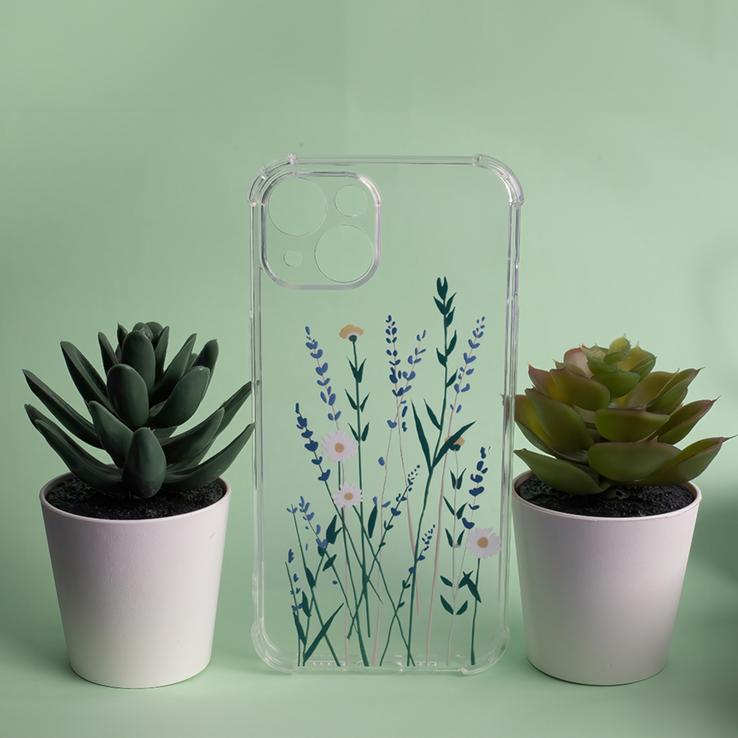 Transparente Handyhülle mit floralem Design, zwischen zwei Topfpflanzen. Grüner Hintergrund.