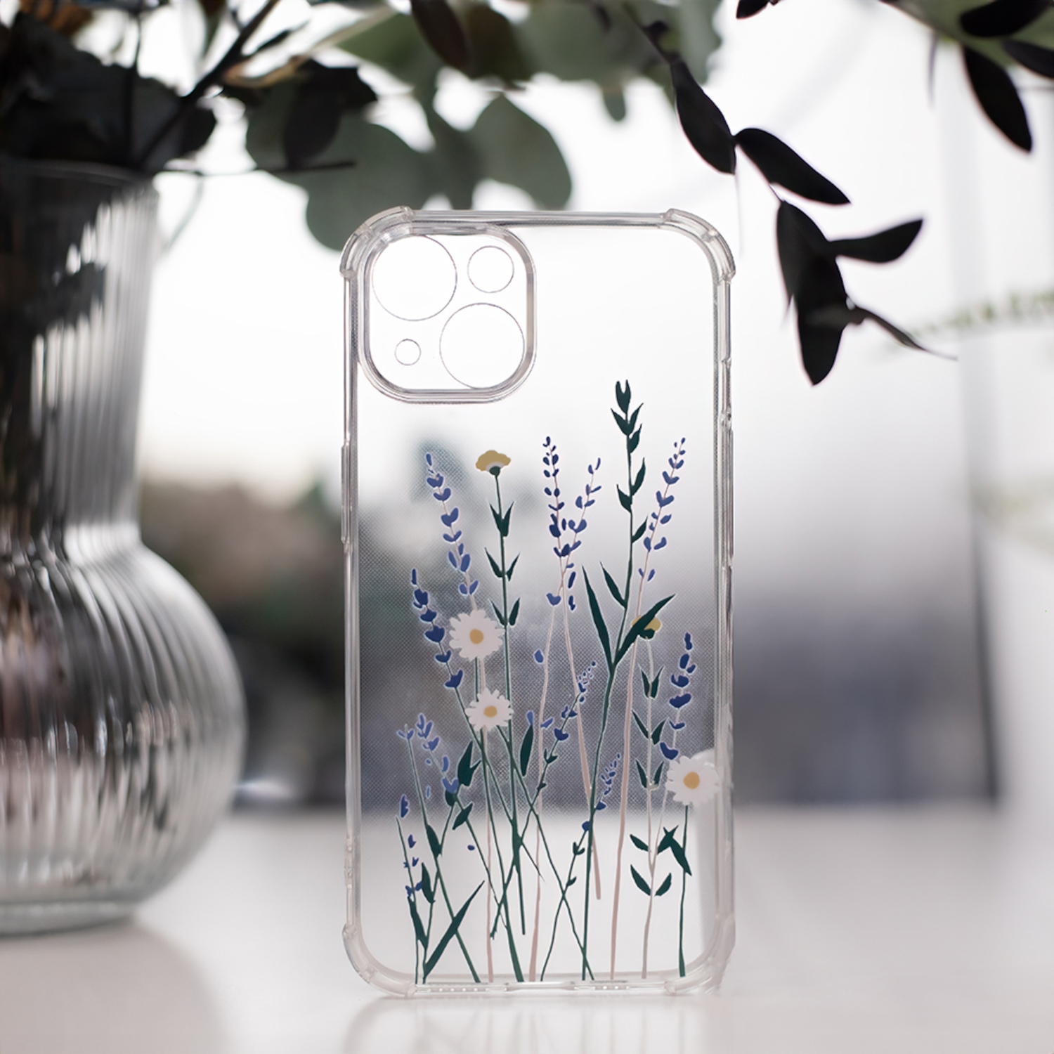 Transparente Handyhülle mit floralem Design. Die Hülle zeigt Blumen und Blätter. Der Hintergrund ist ein Fenster.