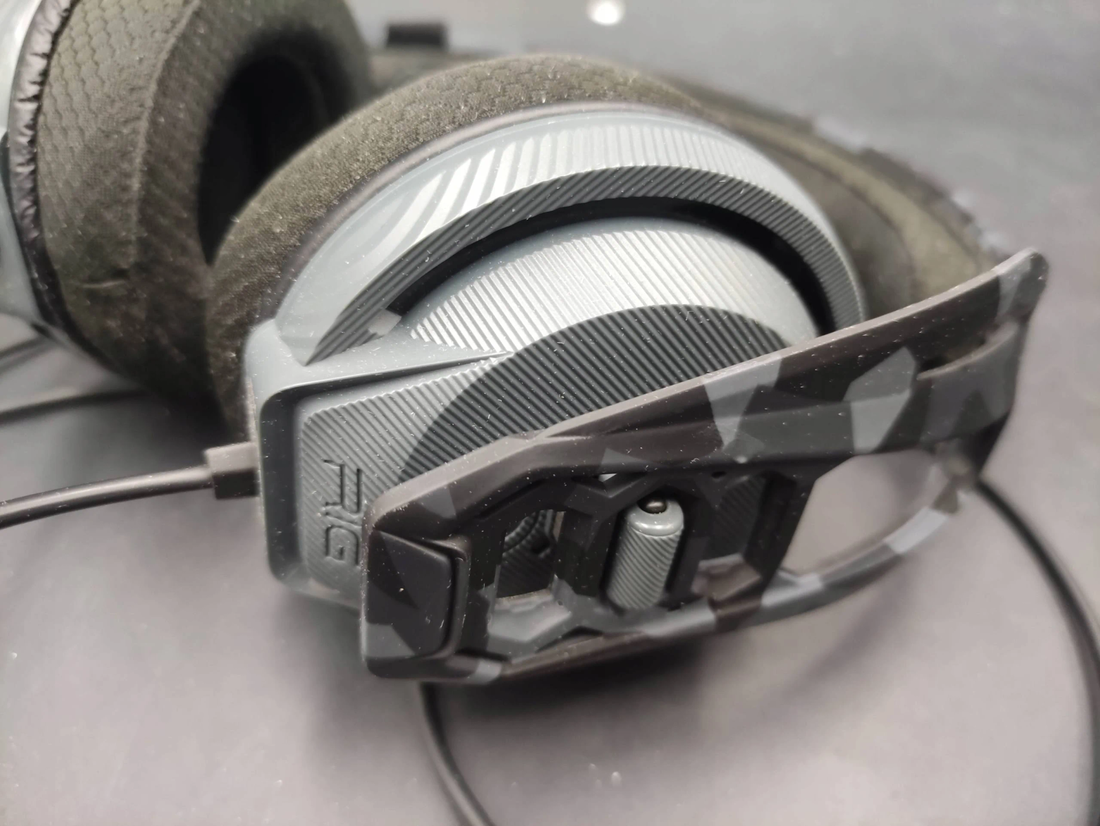 Szare i czarne słuchawki kamuflażowe. Tło to rozmyta, ciemna powierzchnia.