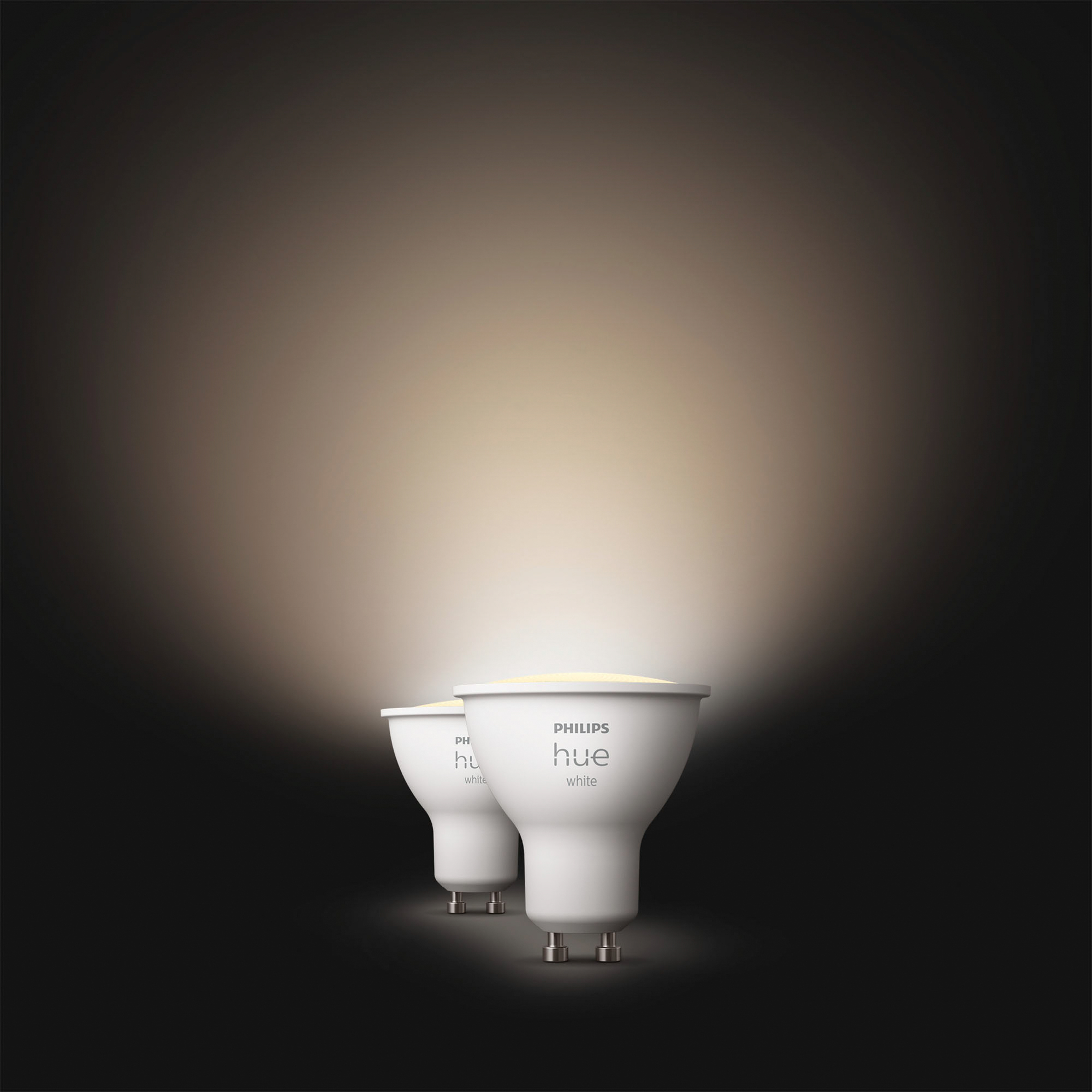 Dwie białe żarówki Philips Hue. Żarówki świecą na ciemnym tle.
