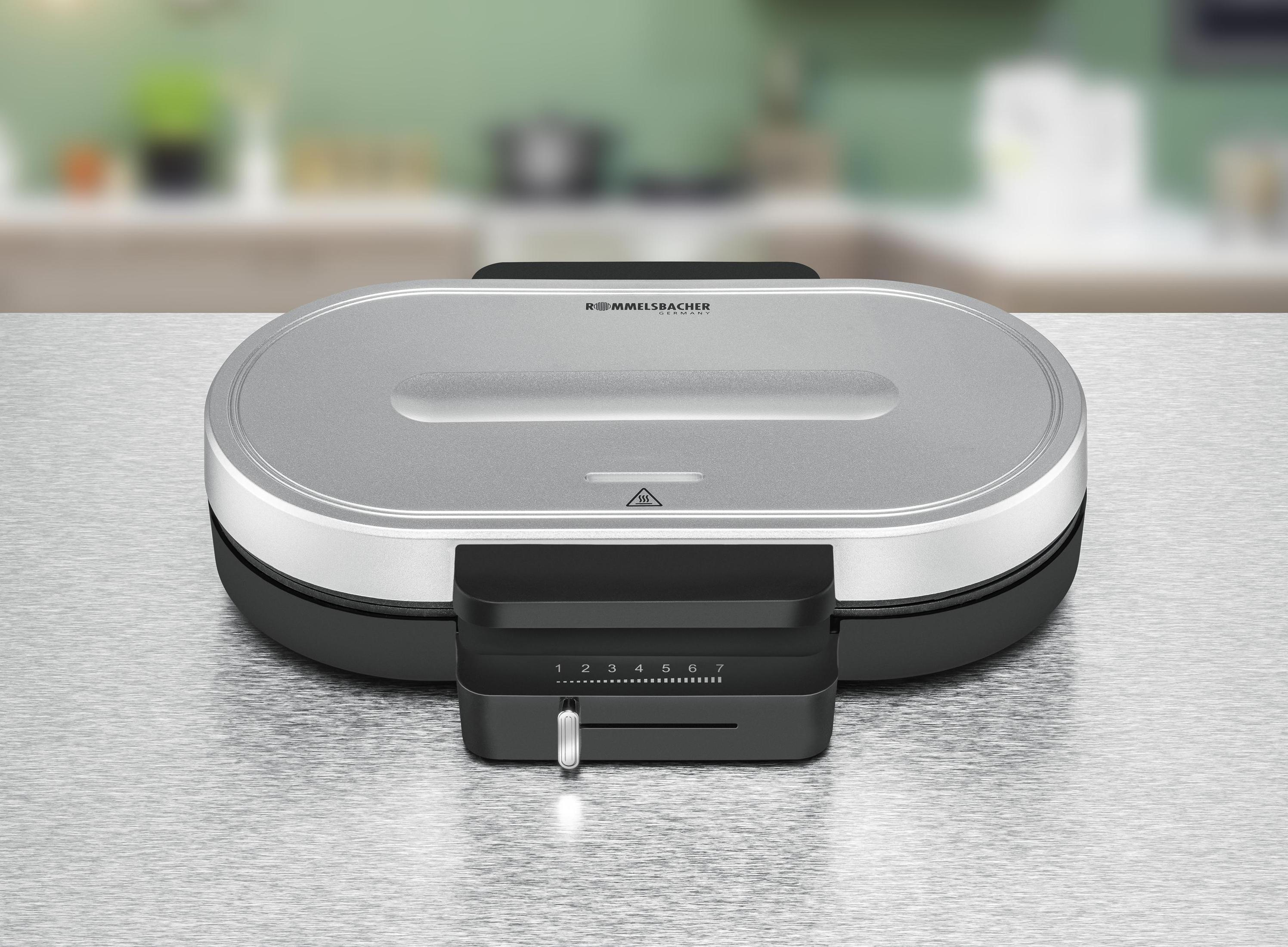 Srebrna gofrownica z czarnym panelem sterowania. Stoi na metalowej powierzchni.