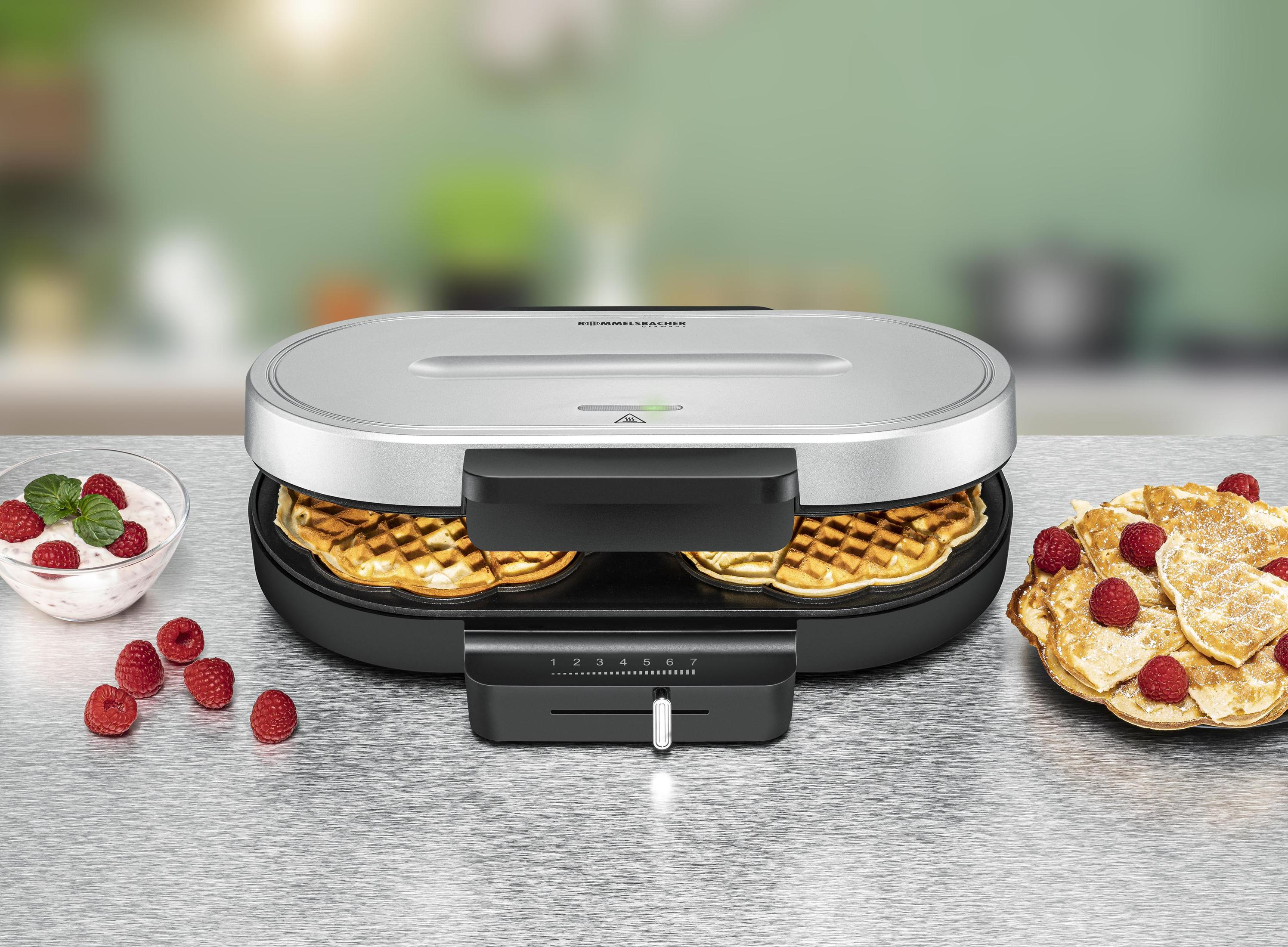 Gofrownica z goframi i malinami. Widoczna miska jogurtu i dodatkowe maliny.