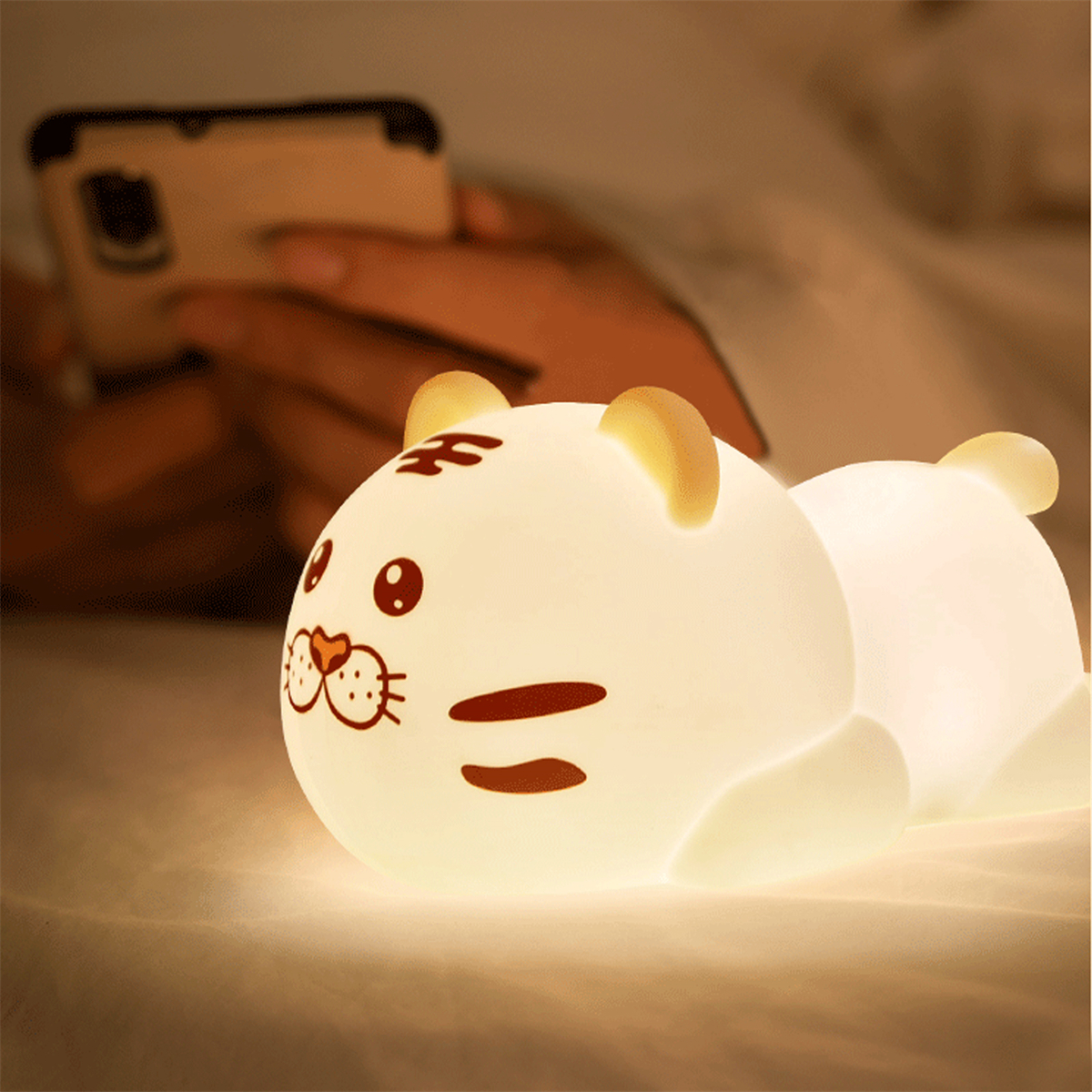 Ein leuchtendes nachtlicht in Tigerform. Eine Person hält im Hintergrund ein Telefon.