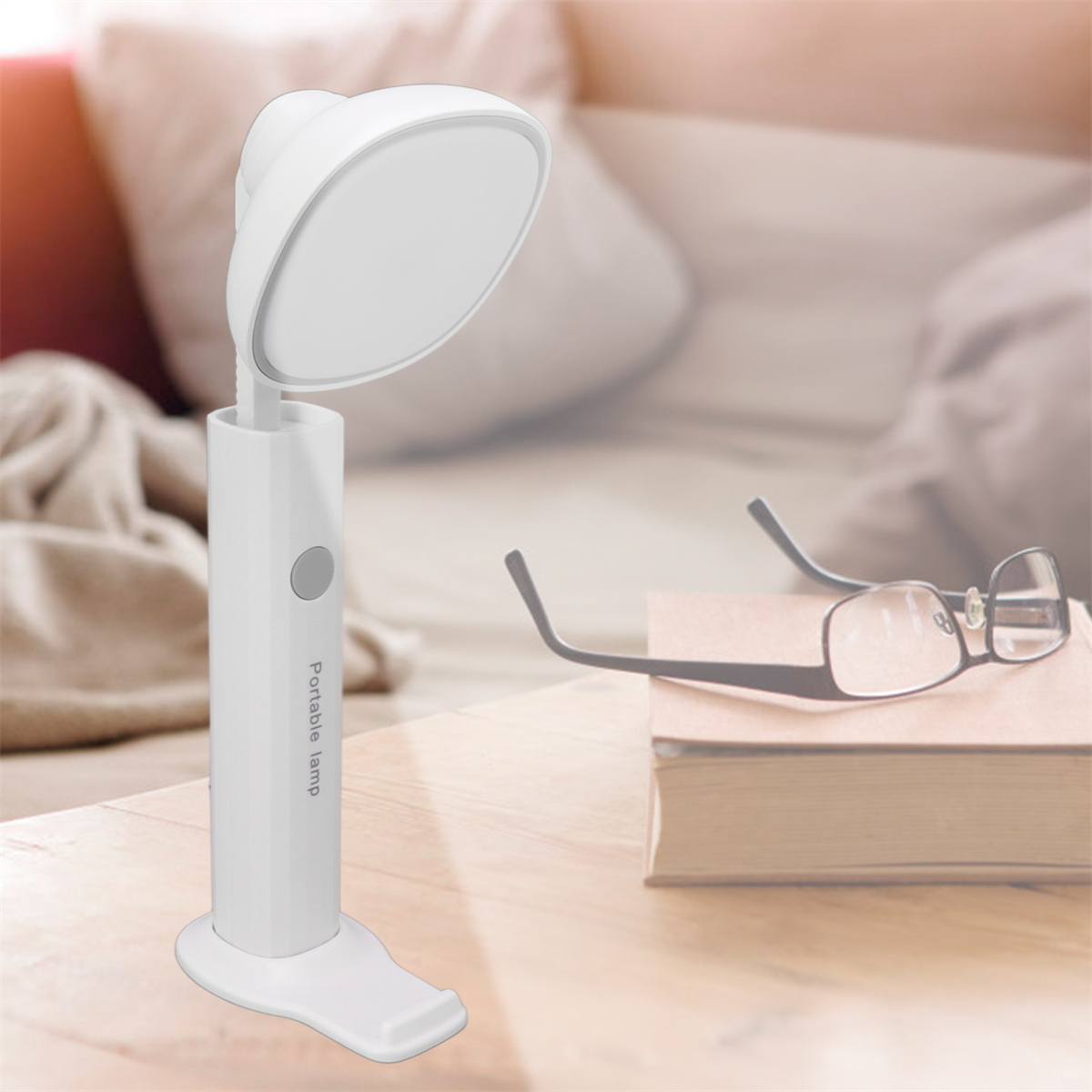 Eine weiße tragbare Lampe und Brille stehen auf einem Holztisch, in der Nähe eines Bettes.