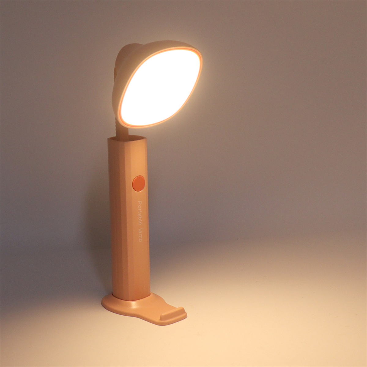 Eine hellpfirsichfarbene Schreibtischlampe mit ovalem Licht und einem einzigen Netzschalter. Sie steht auf einem Ständer.