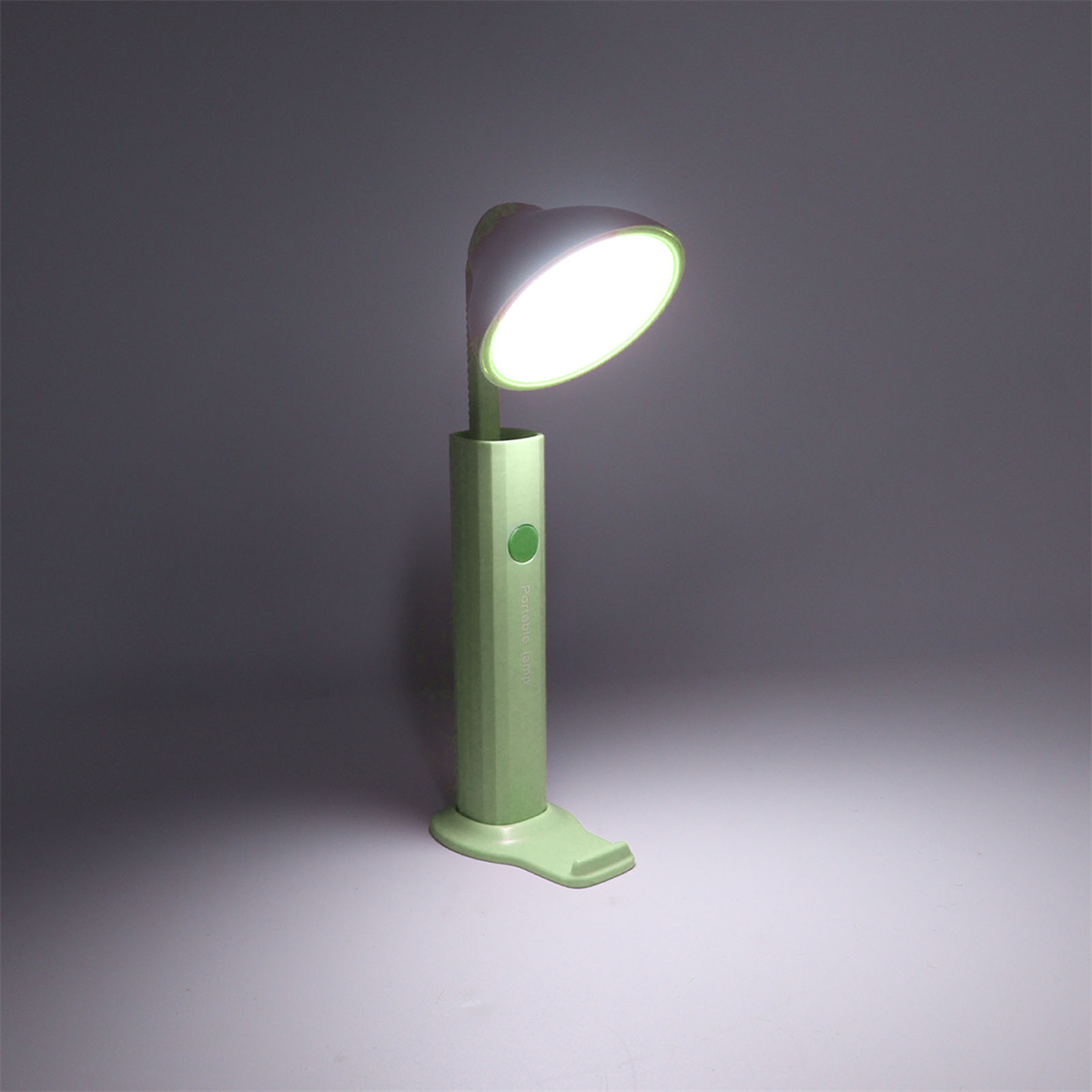Eine grüne Schreibtischlampe leuchtet. Sie hat einen langen, dünnen Körper und einen abgerundeten Leuchtkopf.