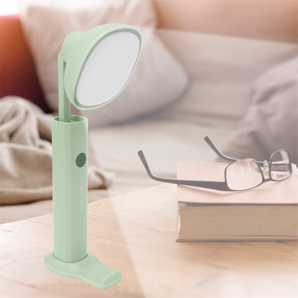 Eine grüne Schreibtischlampe und eine Brille auf einem Holztisch. Weicher Hintergrund und Buch.