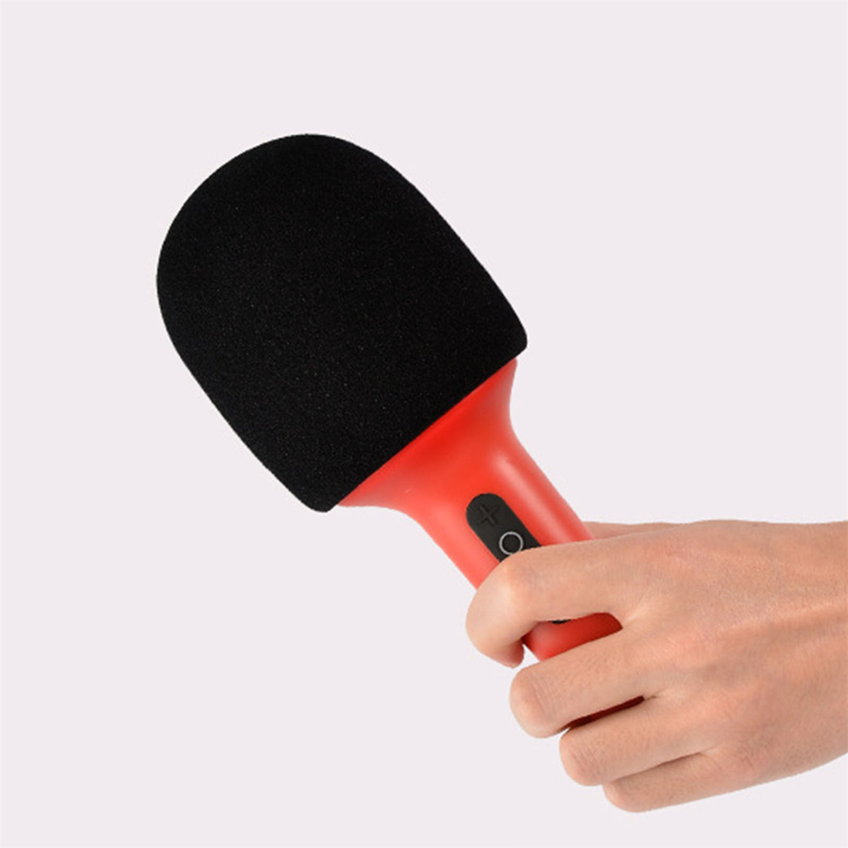 Eine Hand, die ein rotes Mikrofon mit schwarzem Schaumstoffbezug hält. Der Hintergrund ist hellrosa.