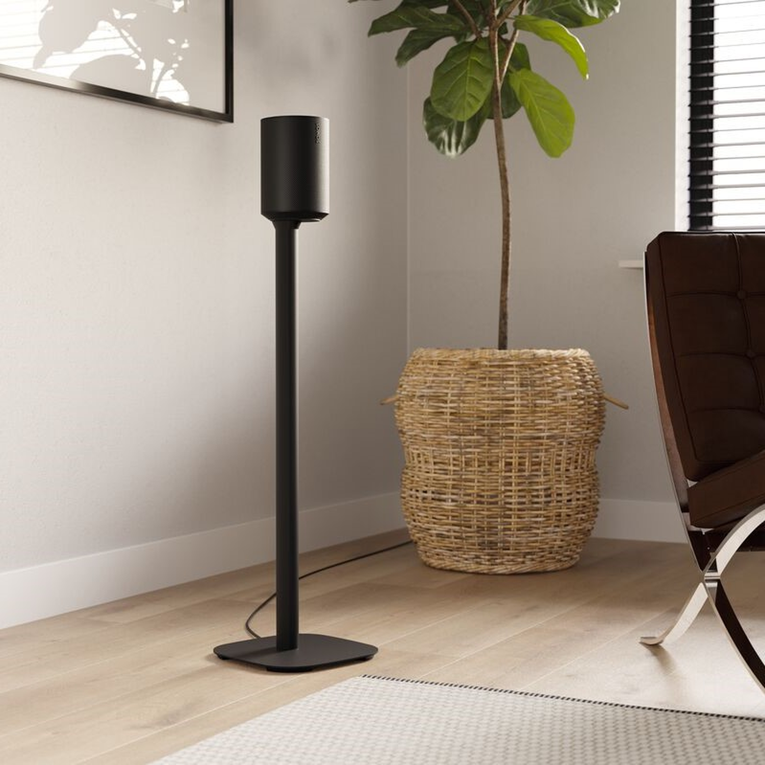 Haut-parleur noir sur pied noir, dans une pièce avec une plante et une chaise marron.