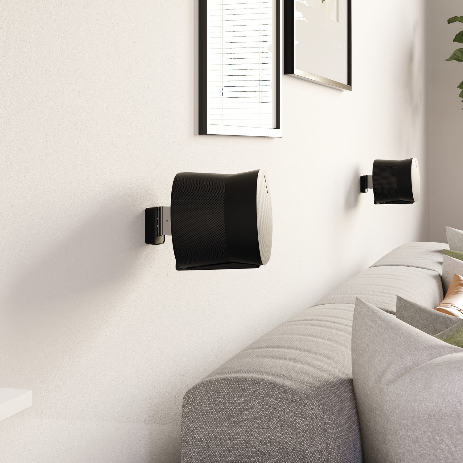 Zwei schwarze Lautsprecher an einer weißen Wand, graue Couch und gerahmte Bilder.