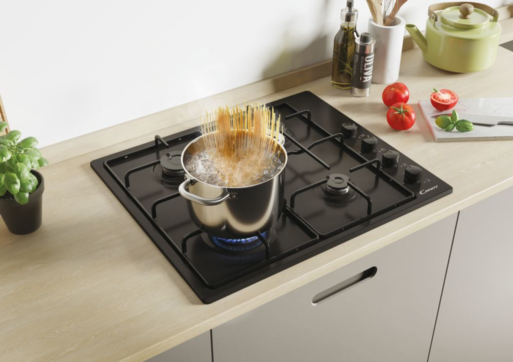 Spaghetti gotuje się w garnku na czarnej kuchence, obok warzywa.