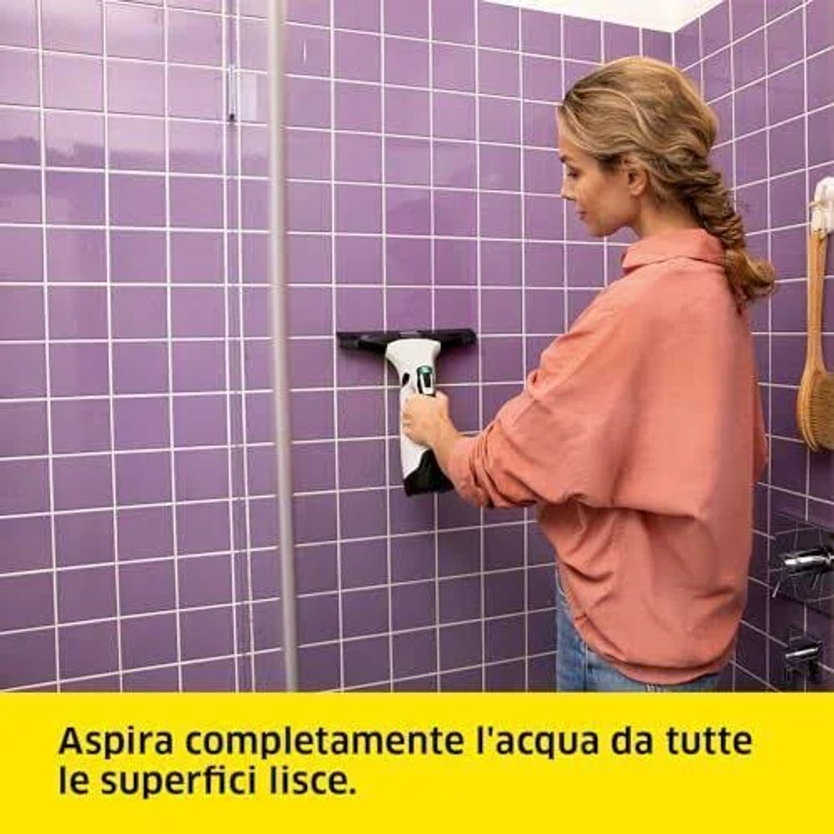 Donna che pulisce la porta della doccia con un tergivetro. Muro di piastrelle viola sullo sfondo. Testo in basso.