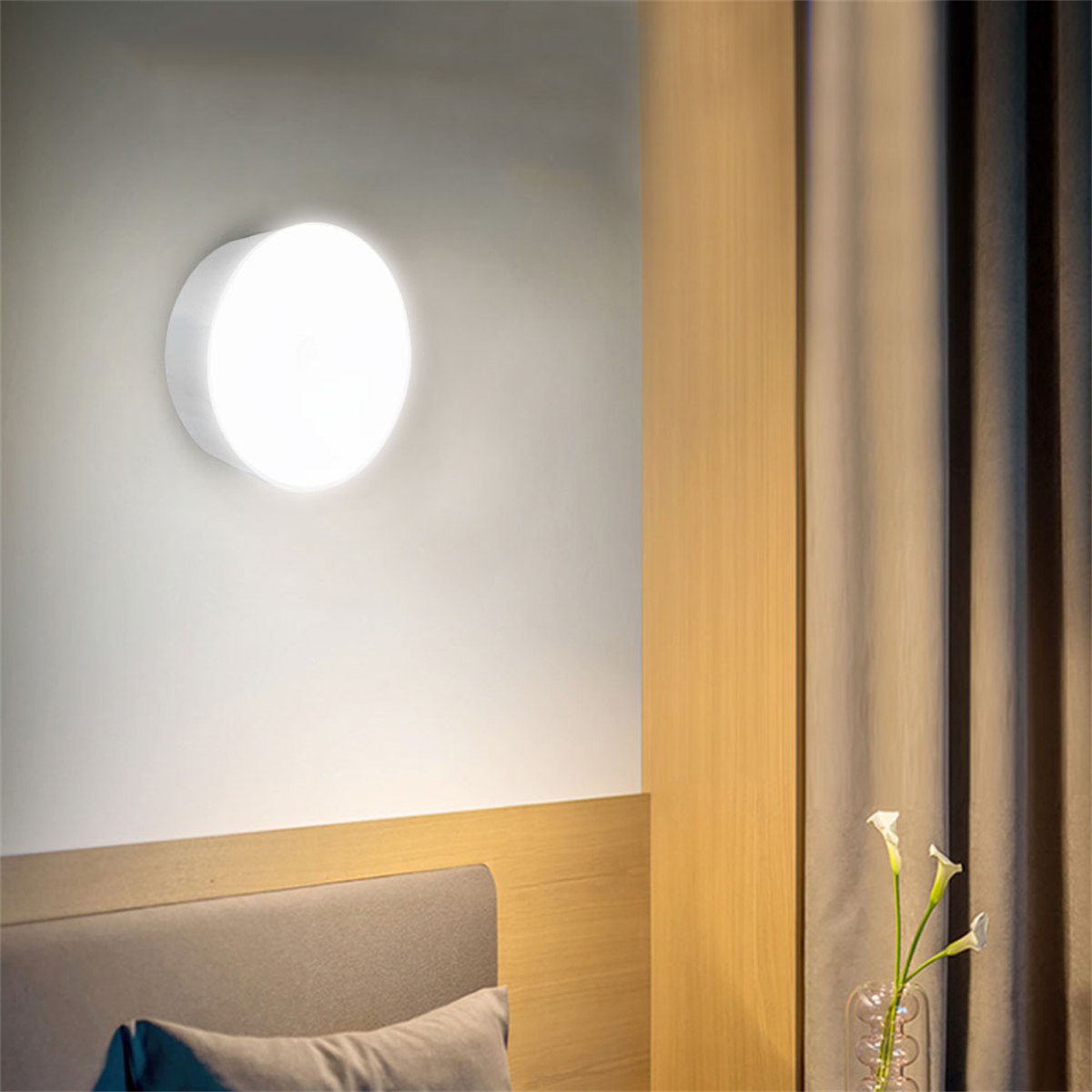 Eine weiße, runde Wandlampe, die Licht aussendet. Die Lampe befindet sich an einer Wand neben einem Vorhang.