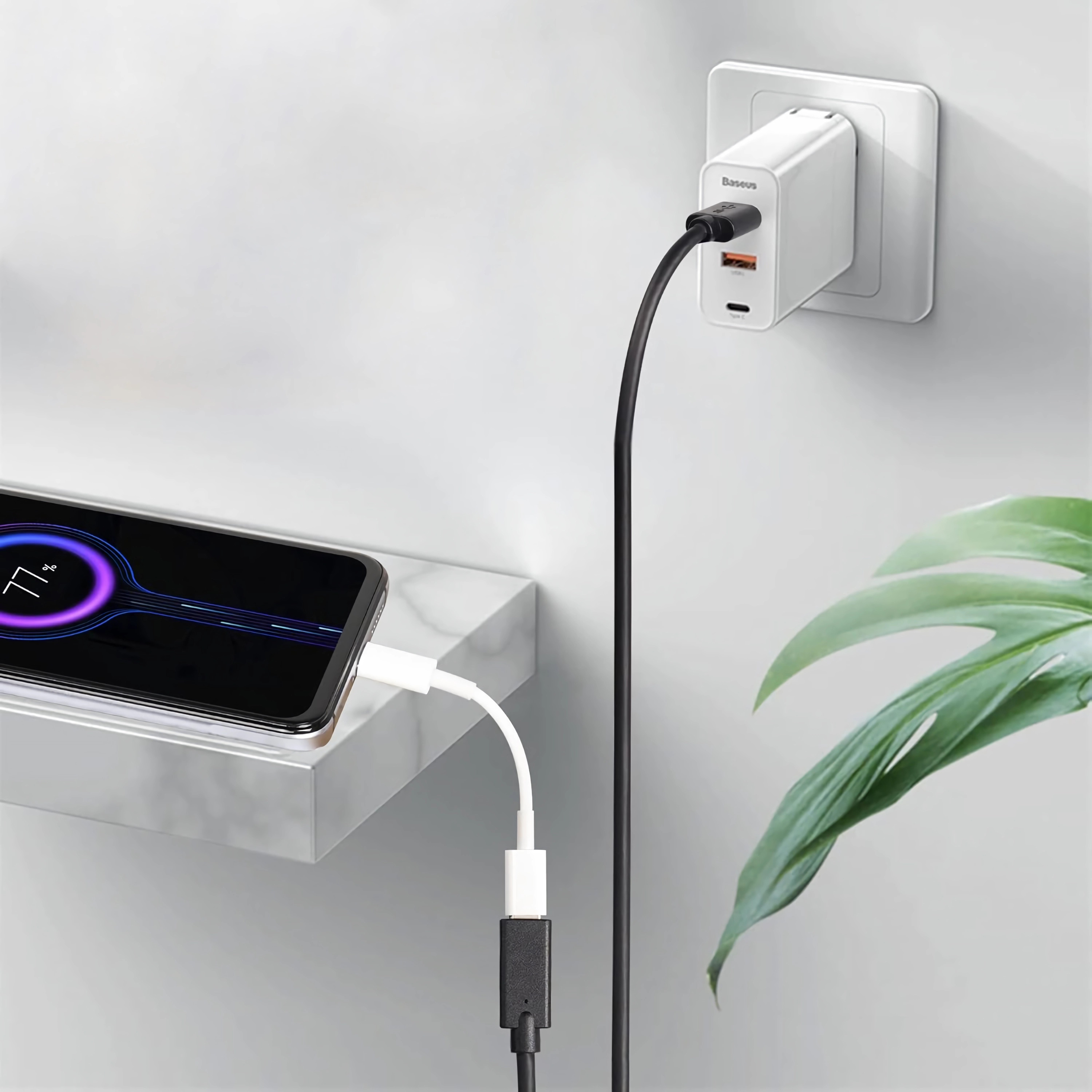 Ein Telefon, das auf einer weißen Oberfläche geladen wird, ein Ladegerät, das an einer Wand angeschlossen ist, und ein schwarzes Kabel.