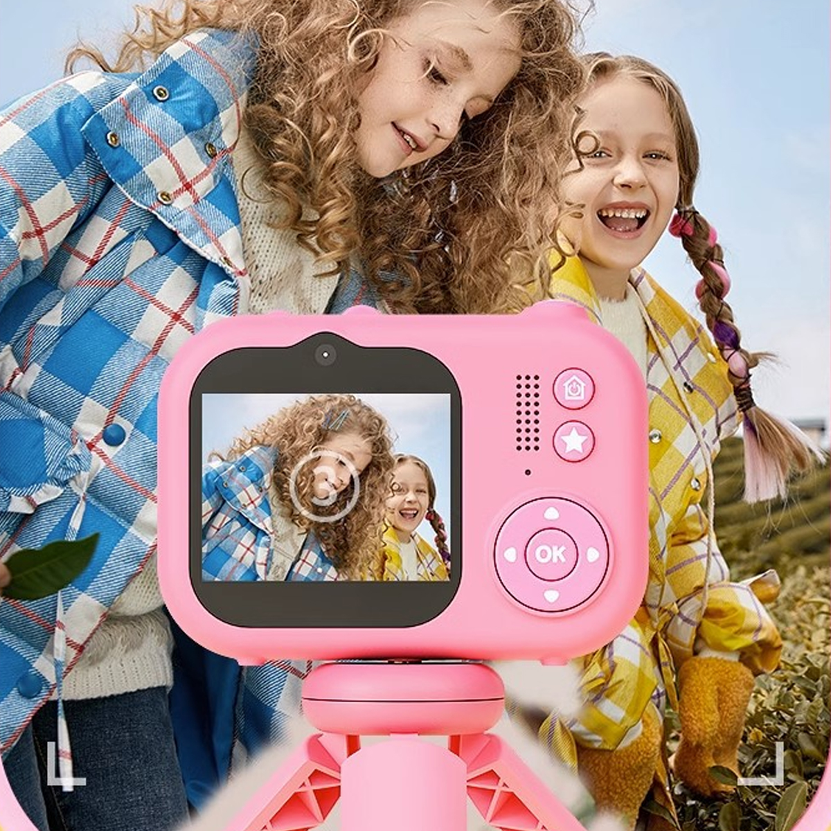 Dwie dziewczyny z różowym aparatem. Jedna się uśmiecha, druga patrzy na aparat.