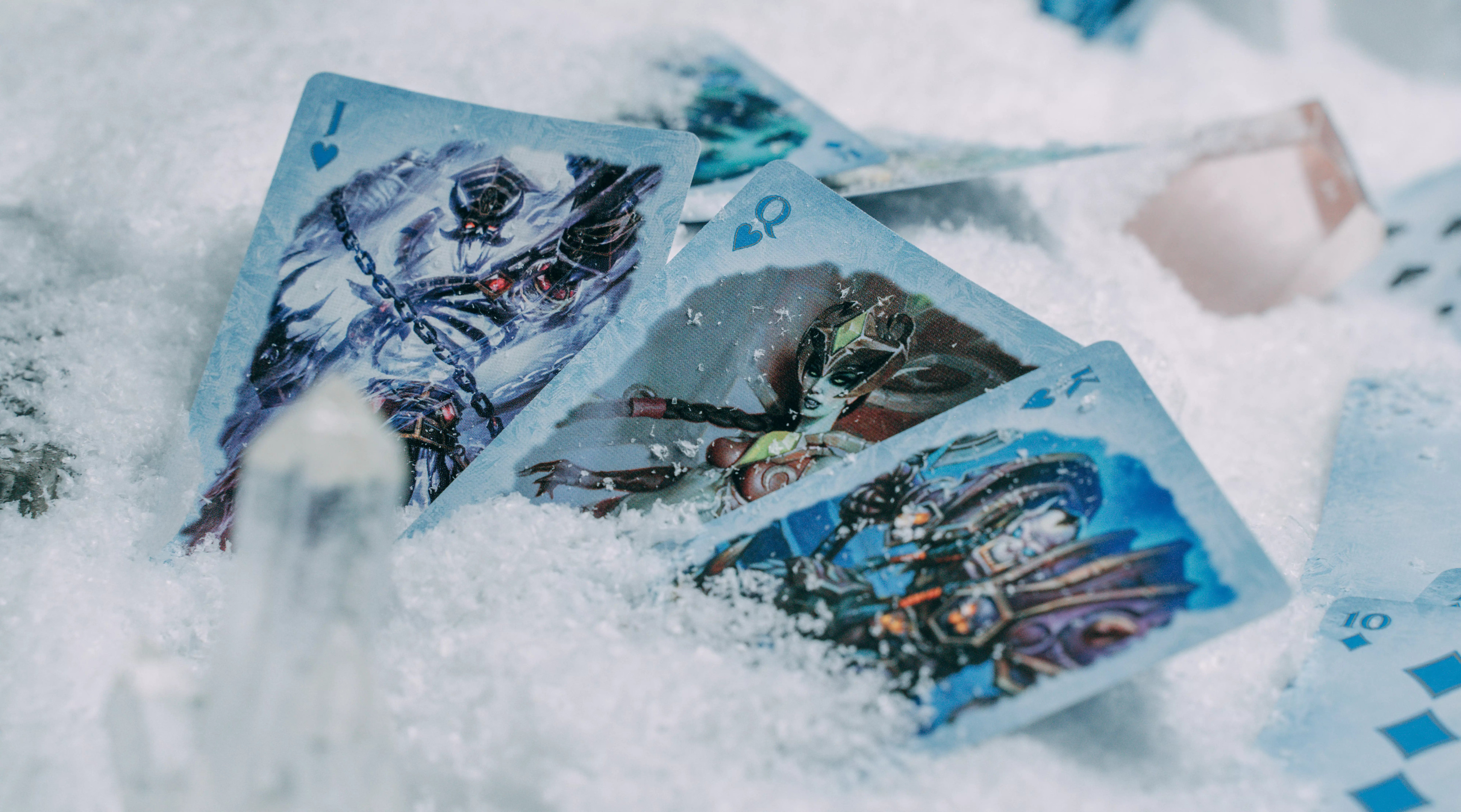 Spielkarten mit Fantasy-Kunst liegen im Schnee, mit einem Kristall.