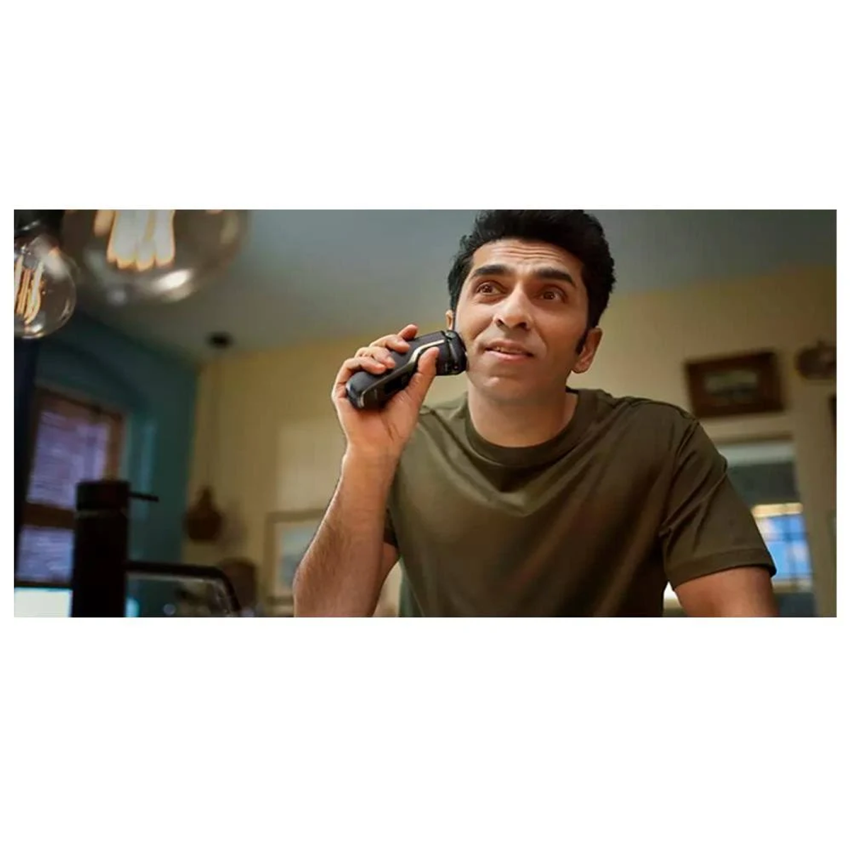 Mężczyzna goli twarz golarką elektryczną. Patrzy w górę z lekkim uśmiechem.