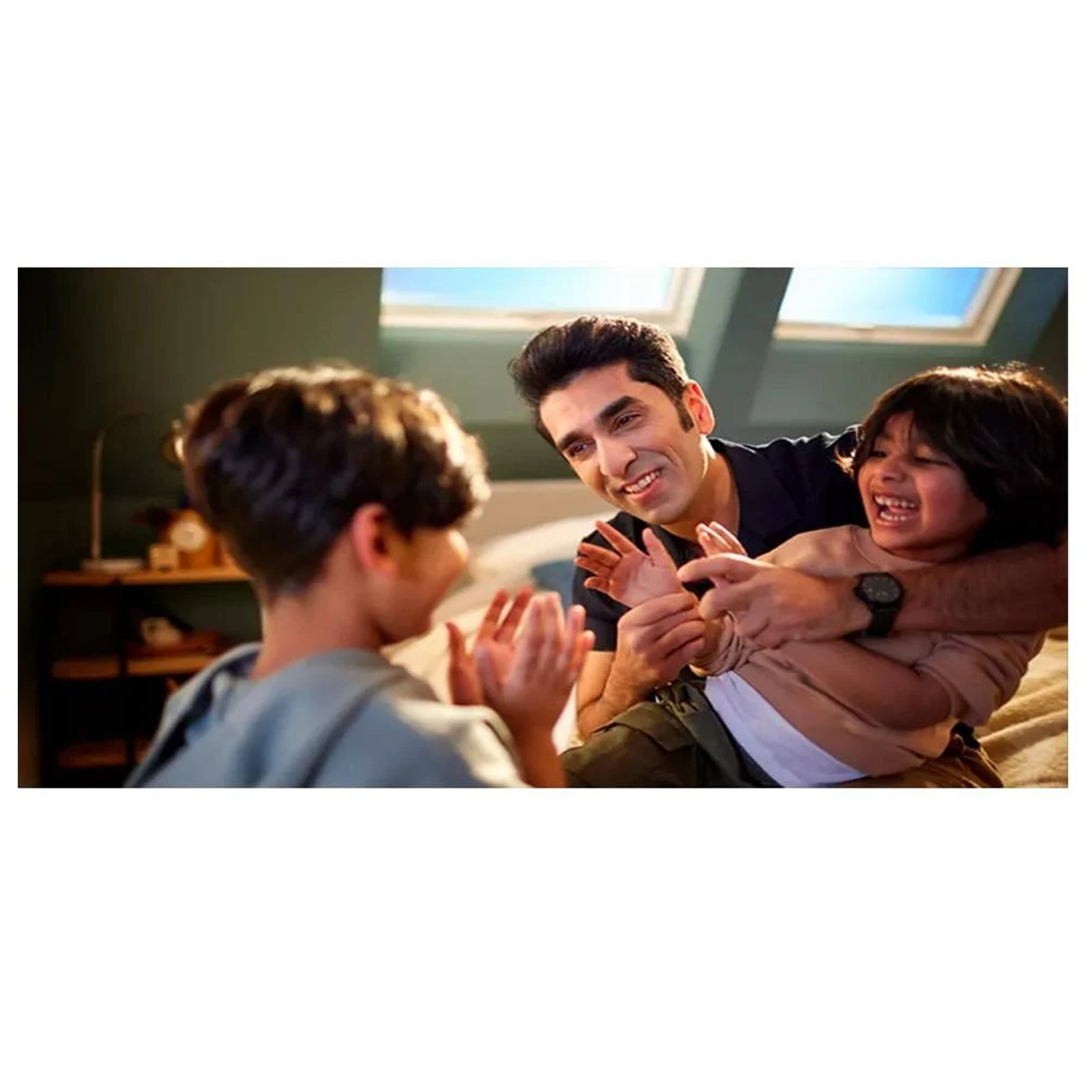 Ojciec bawiący się z dwójką swoich dzieci. Wszyscy się uśmiechają i śmieją. Są w dobrze oświetlonym pokoju.