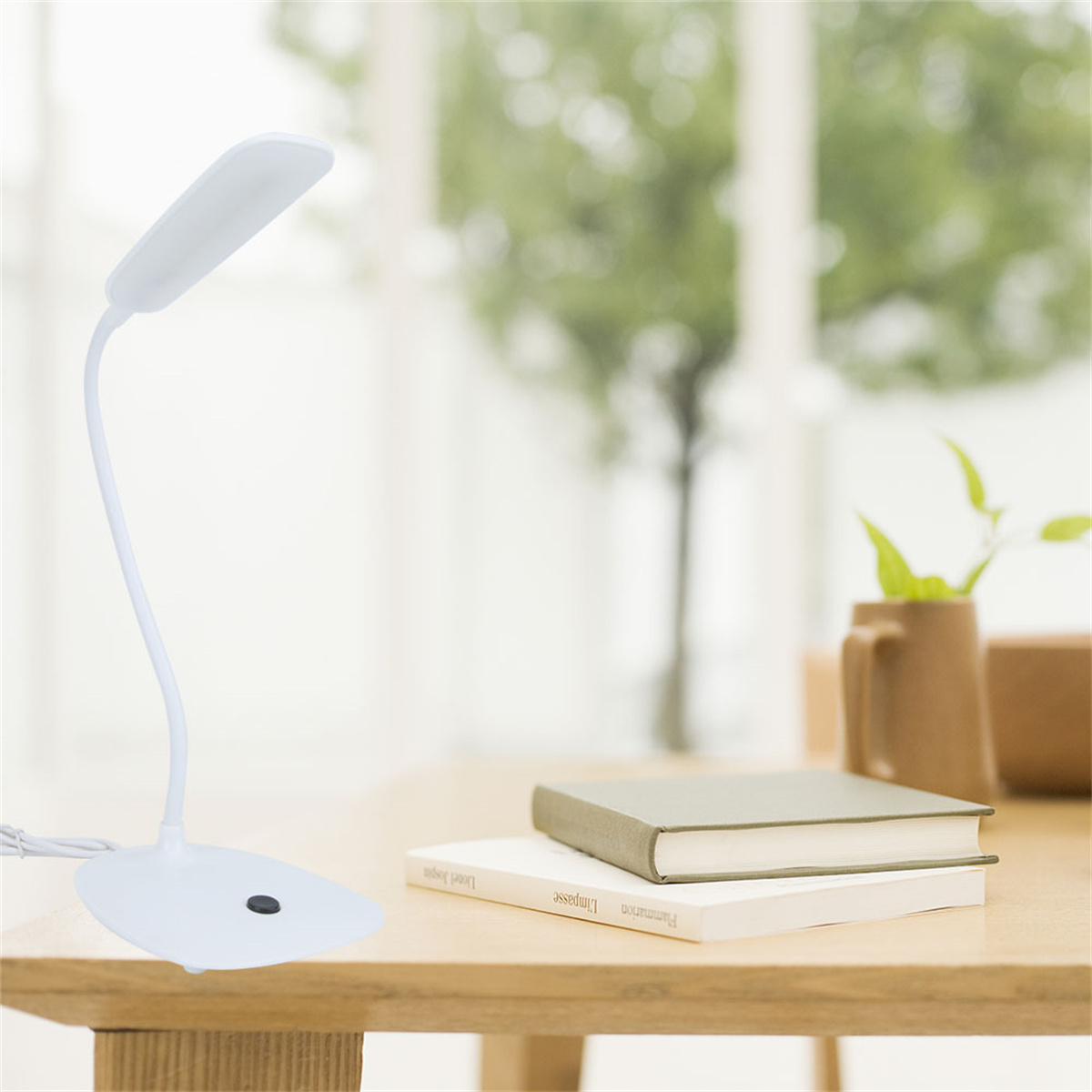 Weiße Schreibtischlampe auf einem Holztisch mit Büchern und Fenster im Hintergrund.