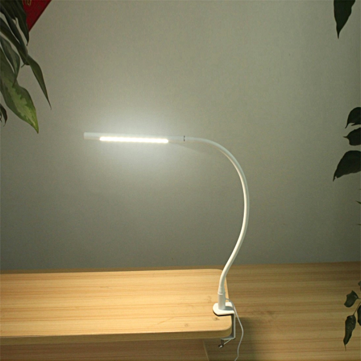 Schreibtischlampe mit weißem, gebogenem Arm, am Tisch befestigt.