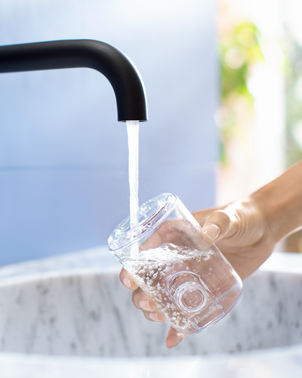 Mano che tiene un bicchiere trasparente sotto un rubinetto con acqua che scorre.