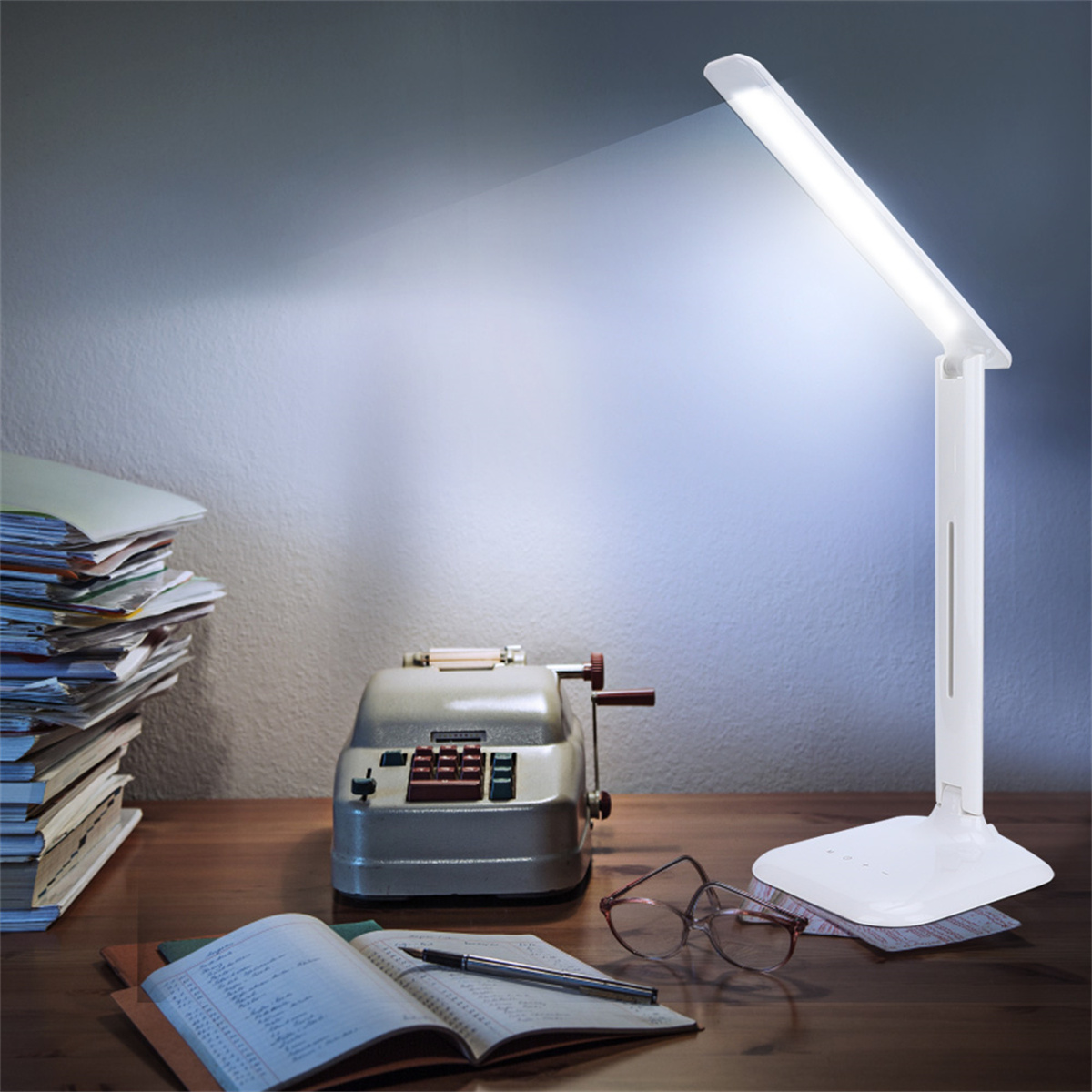Ein Schreibtisch mit einer weißen Schreibtischlampe, Büchern, einem Abakus und einer Brille. Die Lampe ist eingeschaltet und beleuchtet die Szene.