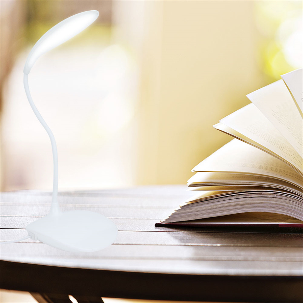 Weiße Schreibtischlampe mit flexiblem Hals, beleuchtet ein offenes Buch auf einem Tisch.