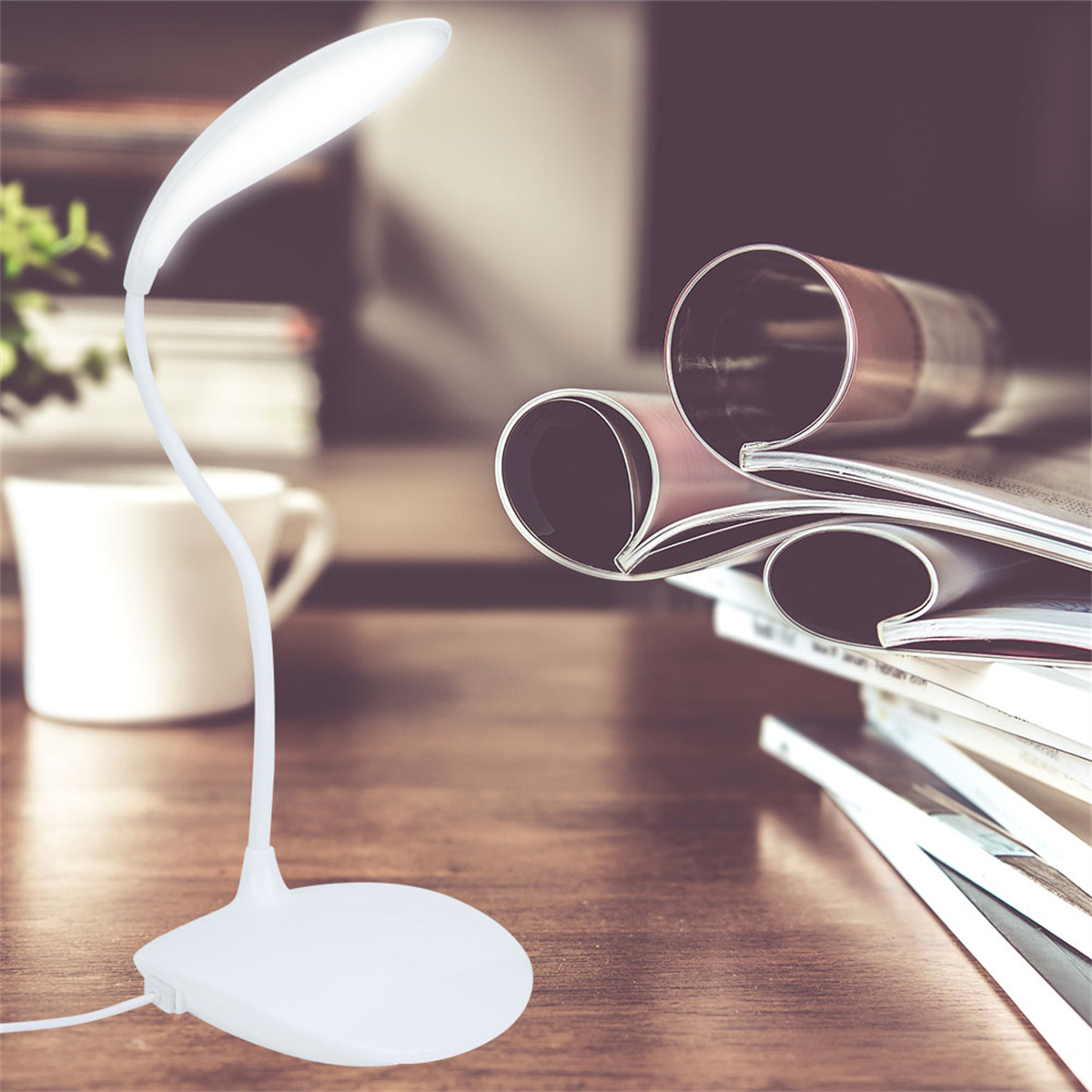 Eine weiße Schreibtischlampe mit gebogenem Hals ist beleuchtet. Rechts liegt ein Stapel Zeitschriften. Hinten steht eine weiße Kaffeetasse.