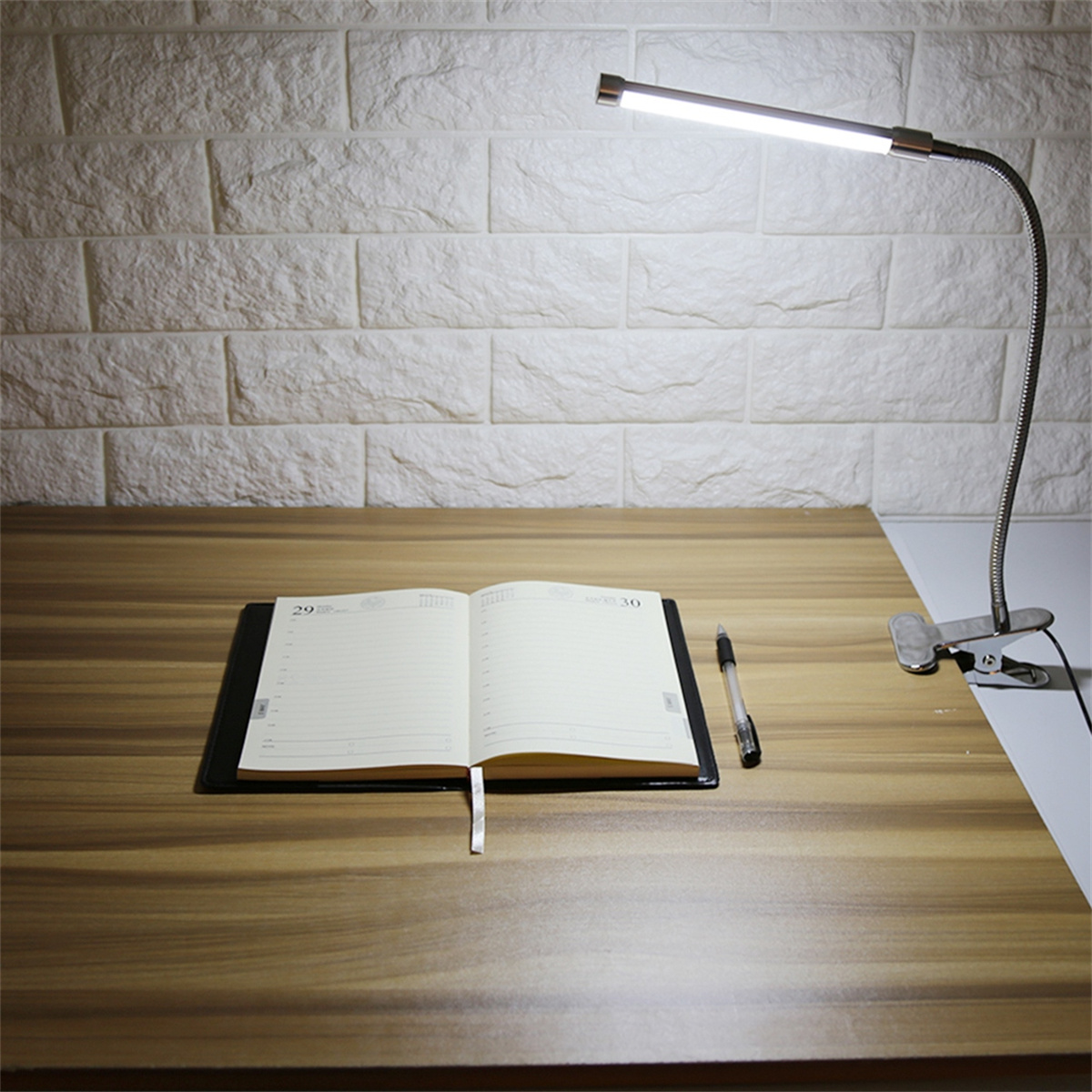 Schreibtisch mit Notizblock, Stift und verstellbarer Lampe. Weiße Ziegelwand im Hintergrund.