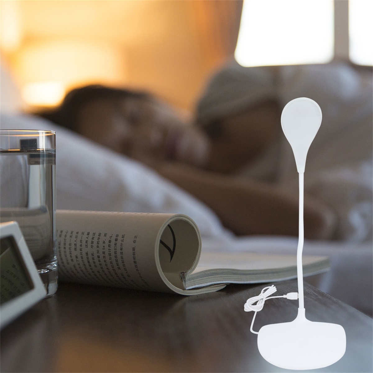 Eine Person schläft im Bett mit einer Lampe und einem Buch auf dem Nachttisch.