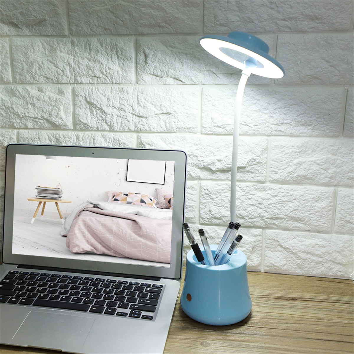 Ein Laptop und eine Schreibtischlampe neben einem hellblauen Stifthalter. Der Bildschirm zeigt ein Schlafzimmer.
