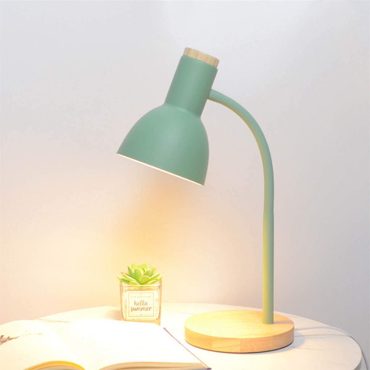 Eine grüne Schreibtischlampe mit Holzfuß, Pflanze und Buch.