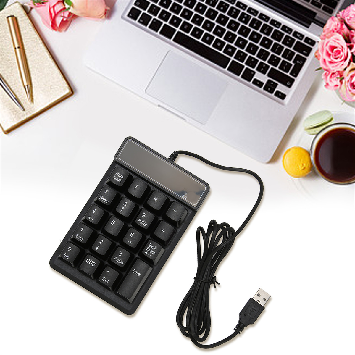 Ein schwarzer Ziffernblock mit Kabel, Notizbuch, Laptop und Rosen auf einem weißen Tisch.