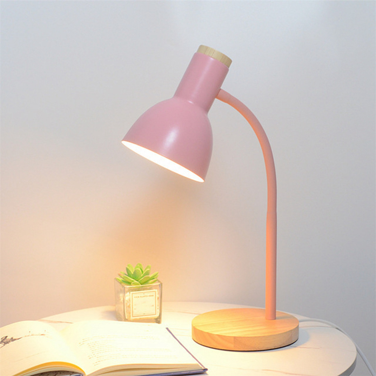 Eine rosa Schreibtischlampe mit Holzsockel und einer kleinen grünen Pflanze.