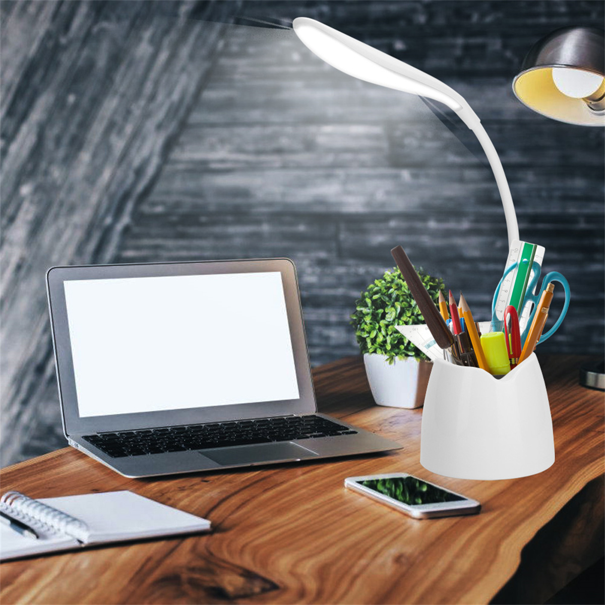 Ein Schreibtisch-Setup mit Laptop, Lampe, Stifthalter, Telefon und Pflanze.