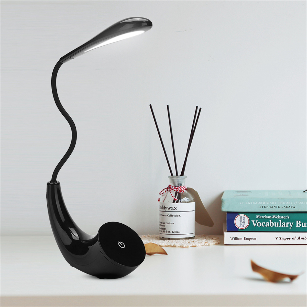 Schwarze Schreibtischlampe mit gebogenem Hals und rundem Sockel. Es gibt Bücher und eine Vase.