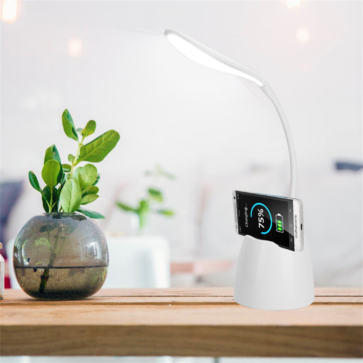 Weiße Schreibtischlampe mit Pflanze und ladendem Telefon. Die Lampe hat einen flexiblen Hals. Holztisch.