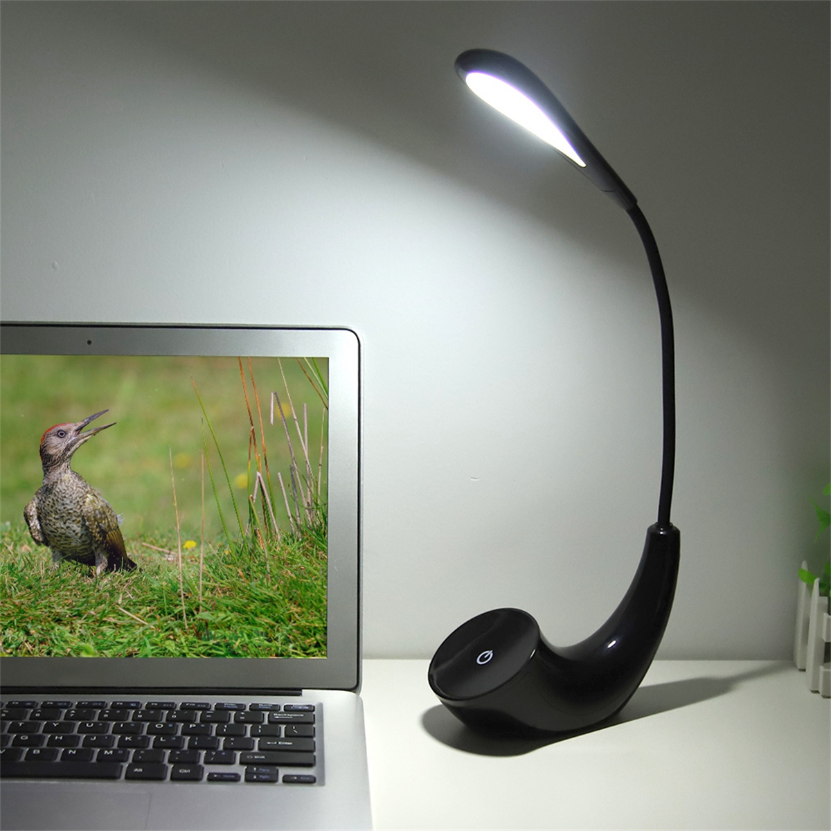 Eine schwarze Schreibtischlampe mit gebogenem Hals. Links ist ein Laptop mit Vogelbild.