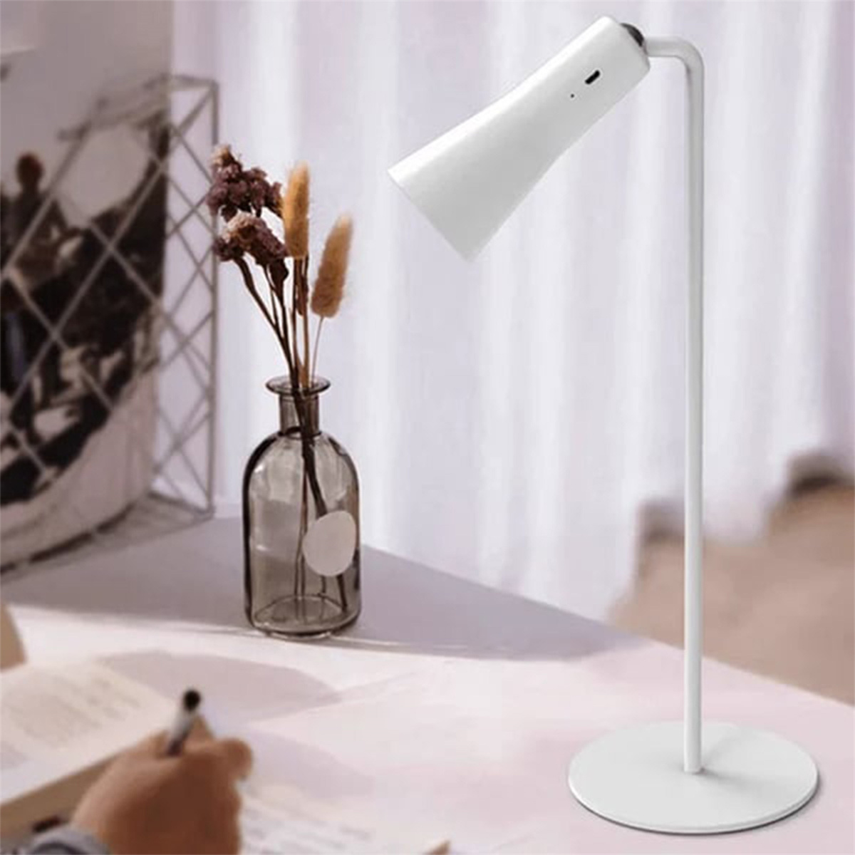 Weiße Schreibtischlampe mit einer Blumenvase auf einem weißen Schreibtisch. Im Hintergrund ein Vorhang.