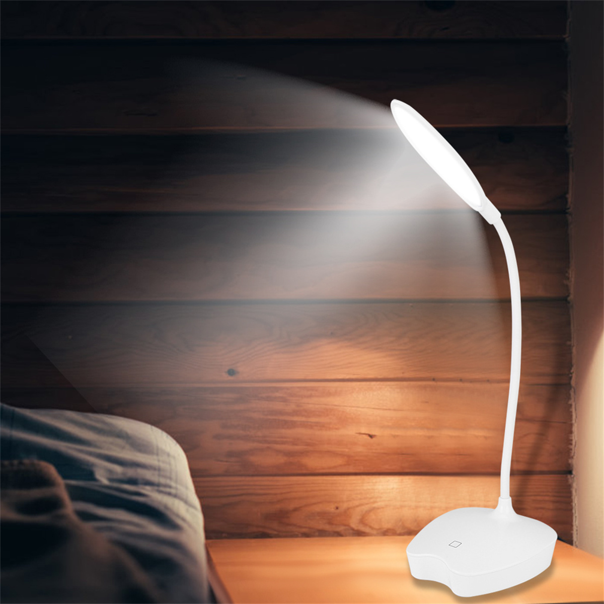 Eine weiße Schreibtischlampe leuchtet auf einem Nachttisch neben einem Bett mit Holz-Hintergrund.