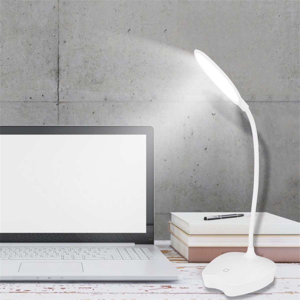 Eine weiße Schreibtischlampe mit biegsamem Hals, neben einem Laptop und Büchern auf einem Schreibtisch.