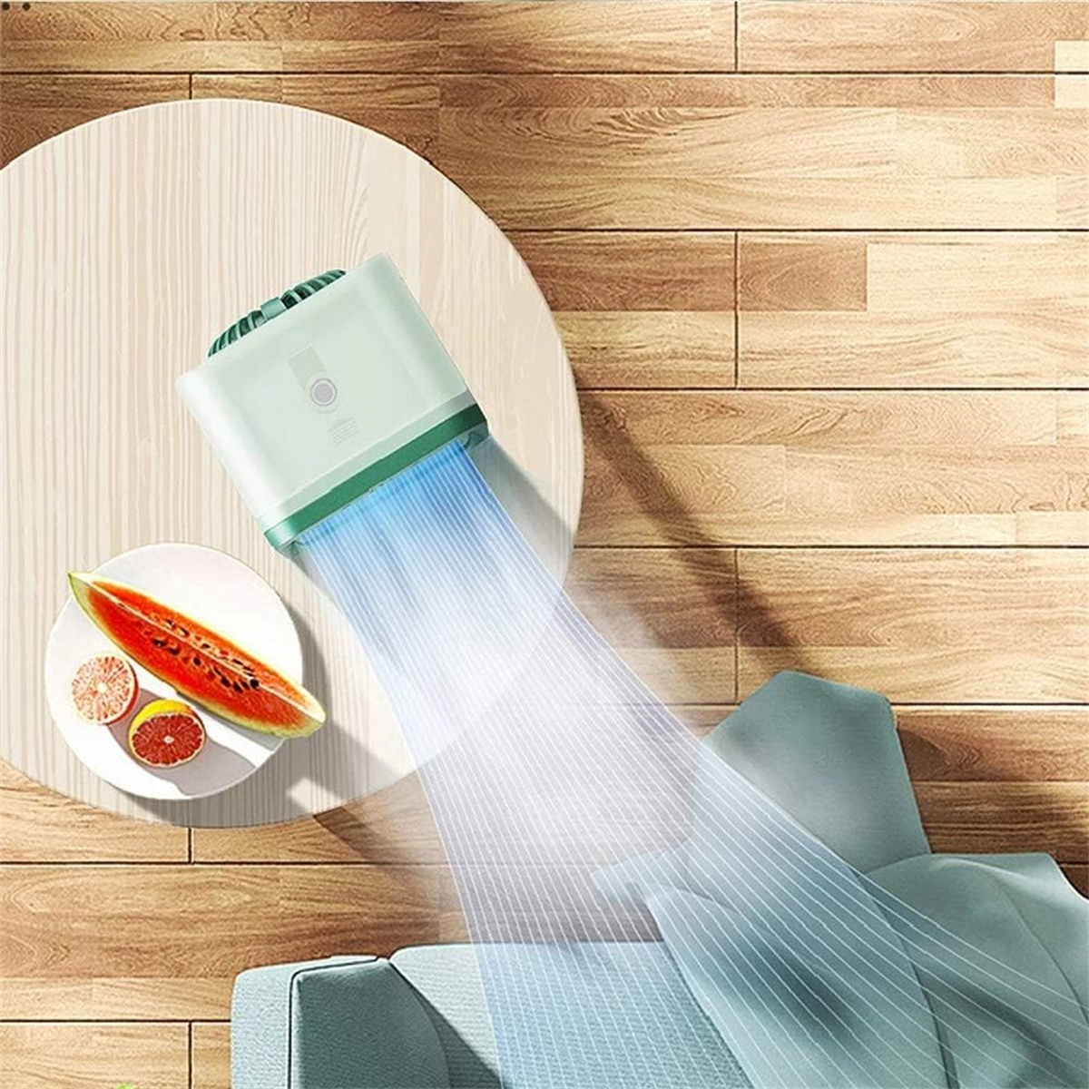 Ein grüner Luftreiniger mit blauem Luftstrom auf einem Holztisch, mit Obst. Hintergrund: ein Holzboden.