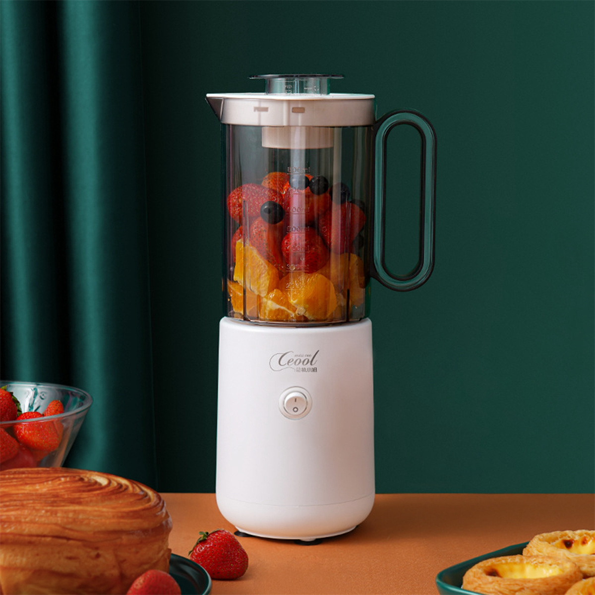 Ein weißer Mixer mit Früchten auf weißer Basis und einem Gebäck.