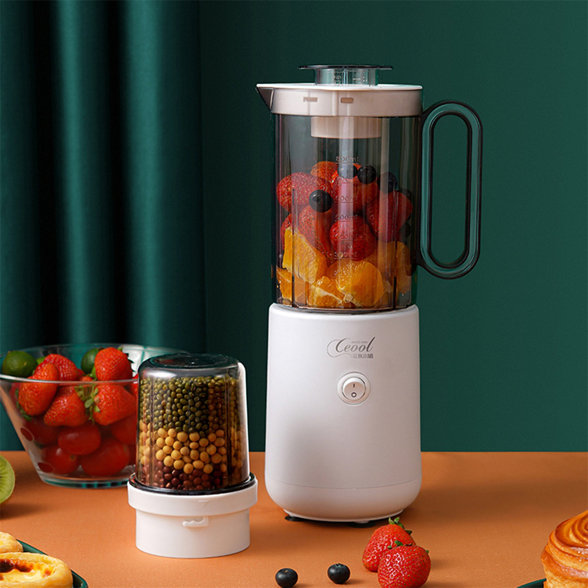 Ein Mixer mit Früchten im Inneren und einem separaten Behälter mit Bohnen. Erdbeeren und Orangen sind sichtbar.