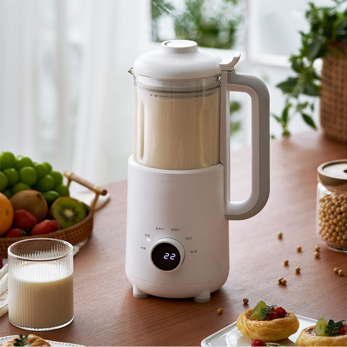 Ein Mixer mit weißer Basis und transparentem Behälter. Der Mixer steht auf einem Holztisch mit Lebensmitteln.