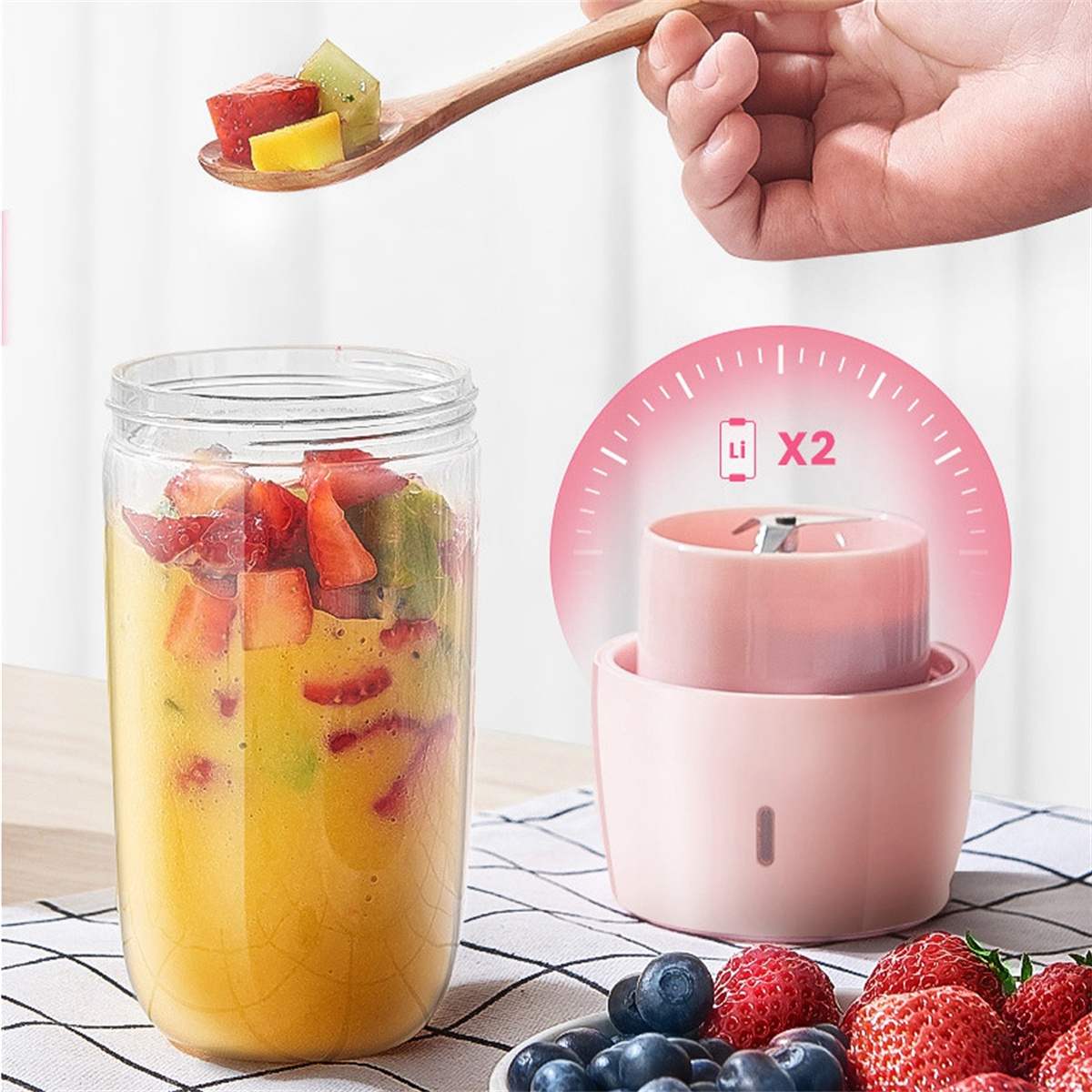 Mixer mit Smoothie-Glas, rosa Basis und Holzlöffel mit Obst. Beeren im Vordergrund.