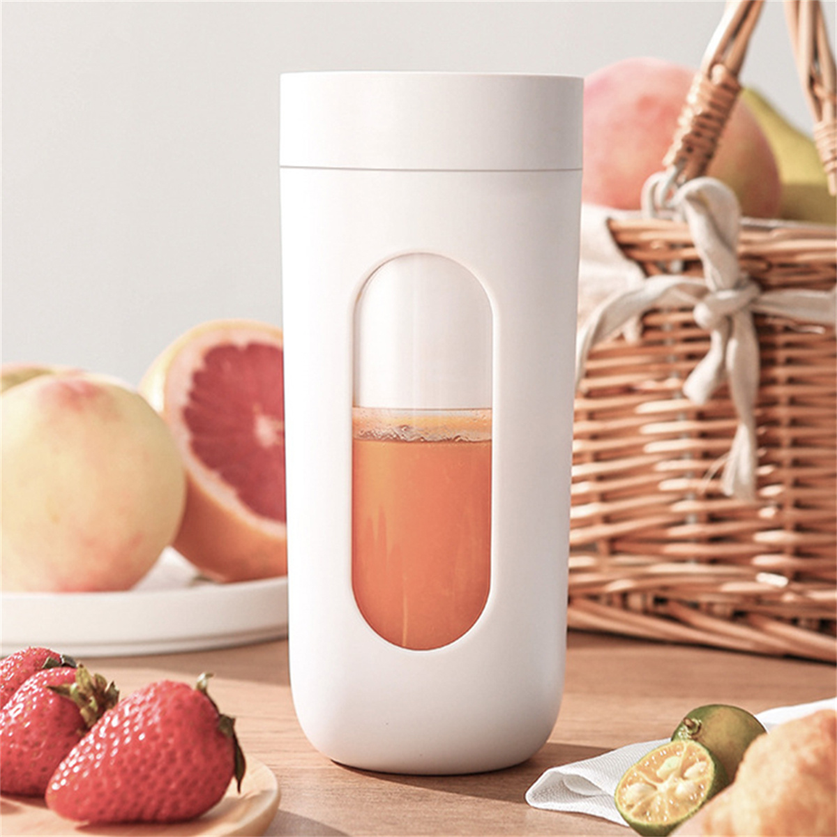 Ein weißer Mixer mit Orangensaft, frische Früchte auf dem Tisch und ein Korb.