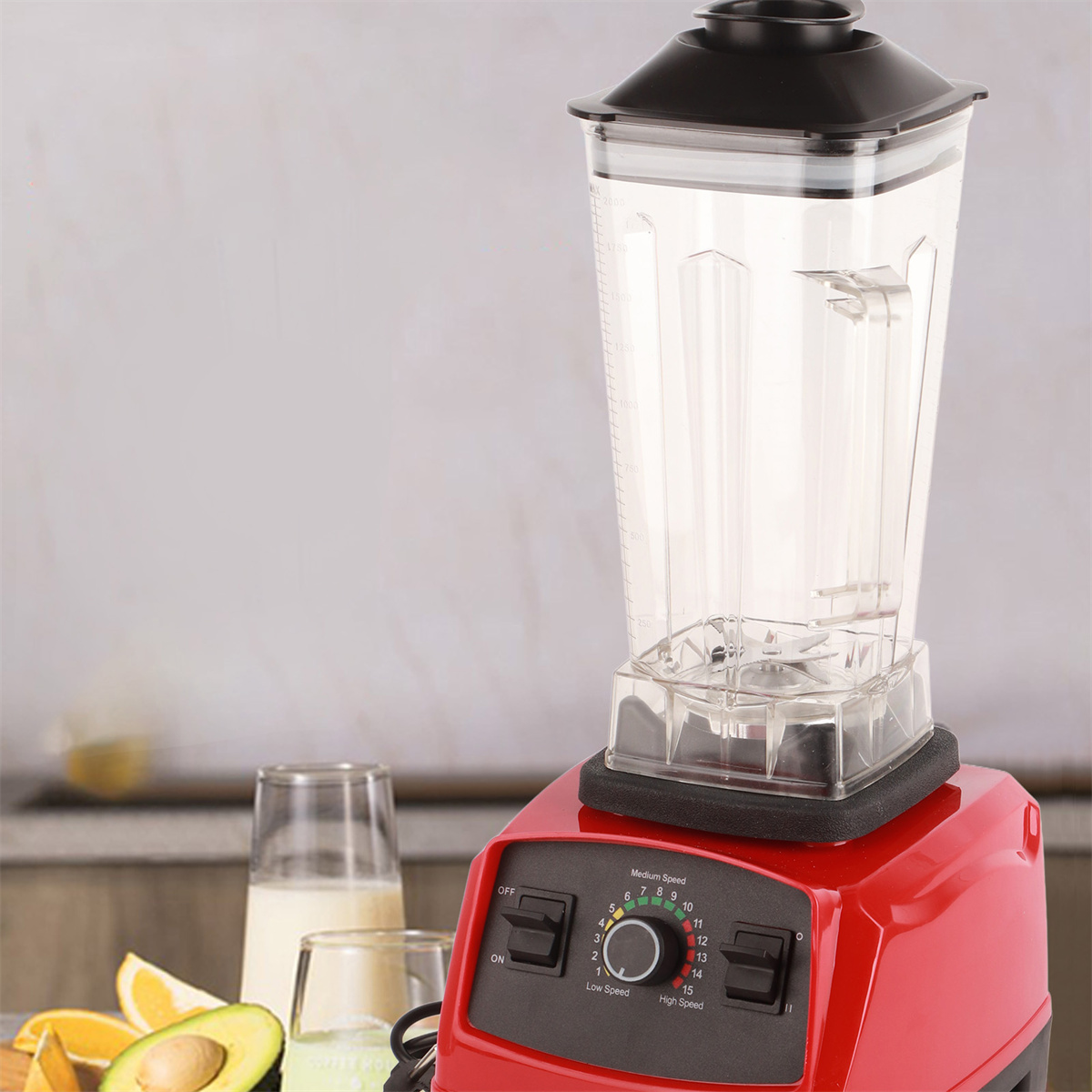 Ein roter und schwarzer Mixer mit einem durchsichtigen Behälter. Daneben Zutaten: Avocado und Orangen.