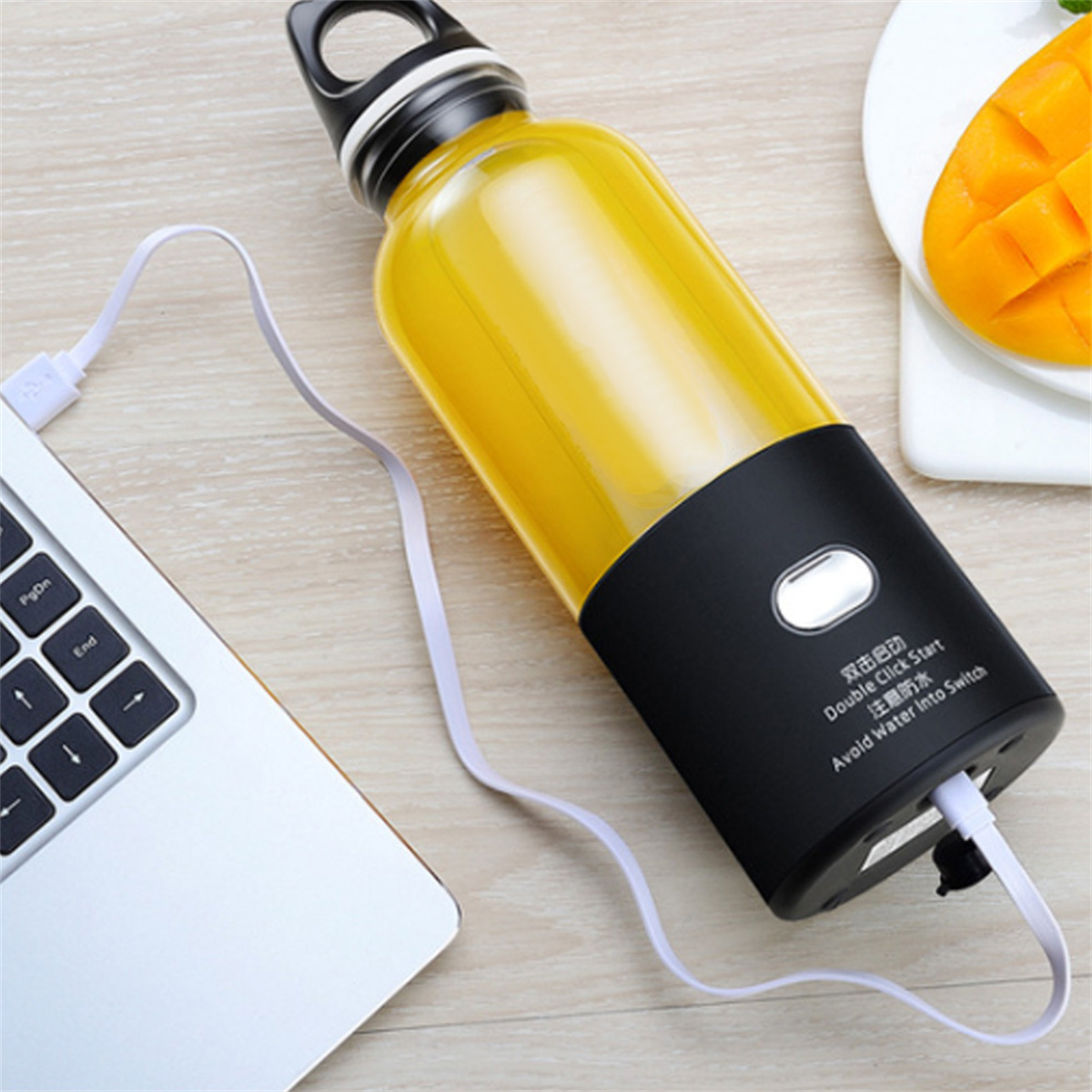 Ein tragbarer Mixer mit gelber Flüssigkeit steht neben Laptop und Mango. Der Mixer ist schwarz.